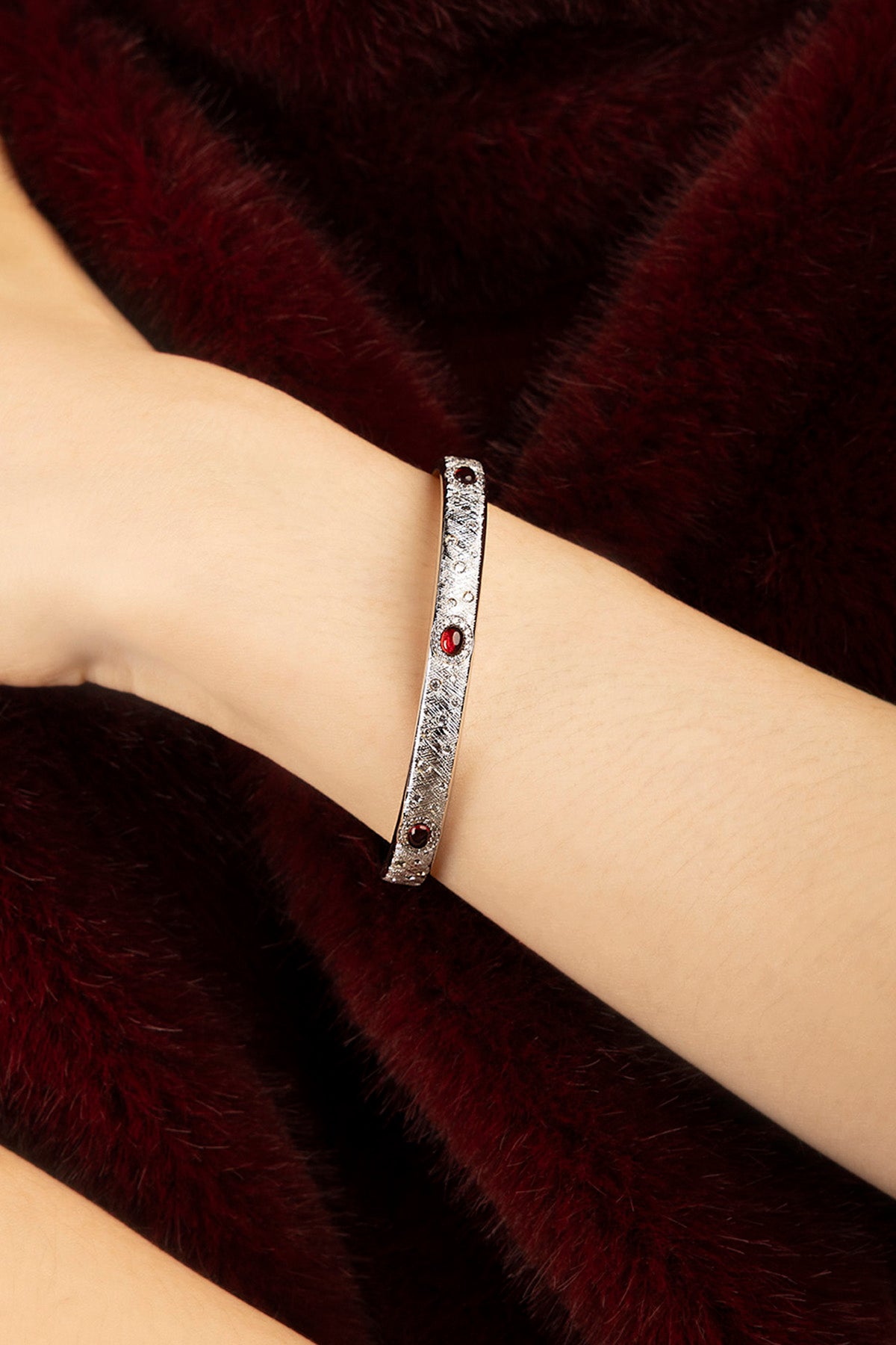 Woman wearing APM bangle, rhodium finish glowing against velvet warmth, quietly bold.