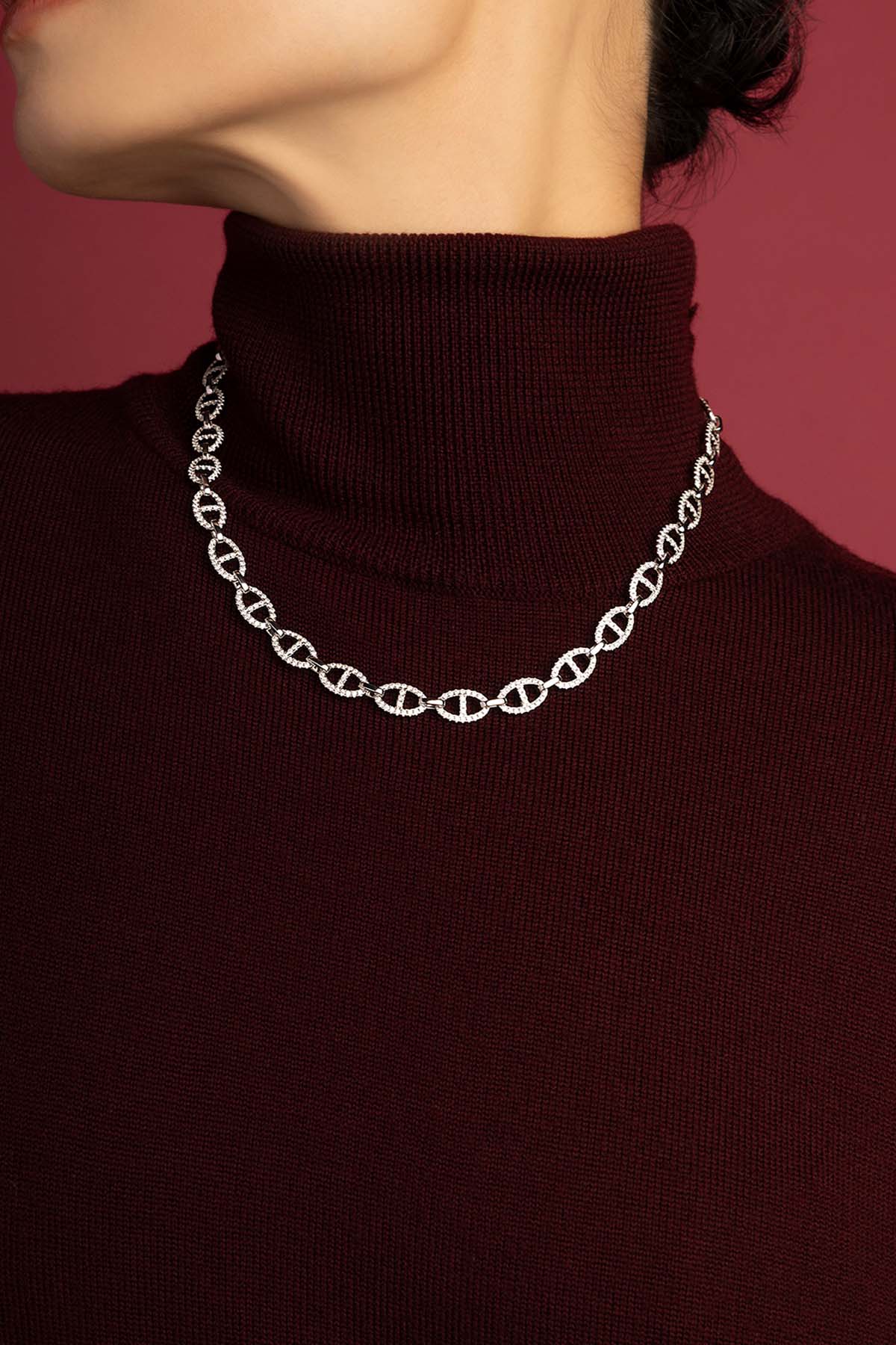 Woman wearing APM Morse Necklace, sculpted links shimmering against burgundy elegance.