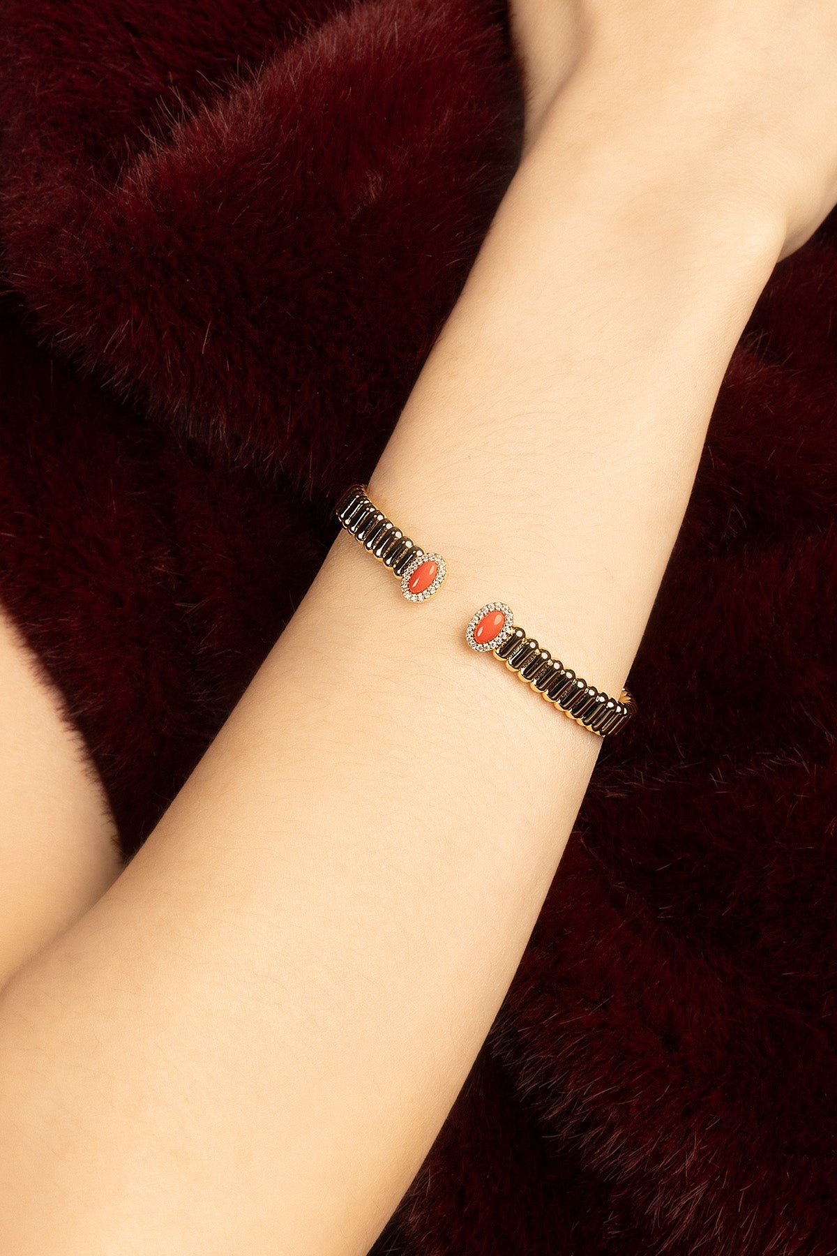 Woman wearing APM Monaco bracelet, coral accents glowing against velvety warmth.