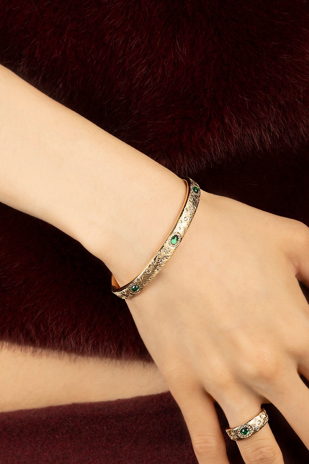 Woman wearing APM Monaco bangle, golden allure with emerald sparks, quietly regal.