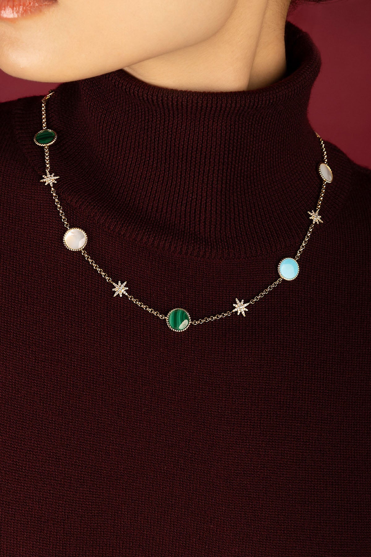 Woman wearing APM Monaco necklace, a celestial dance of colors on burgundy.