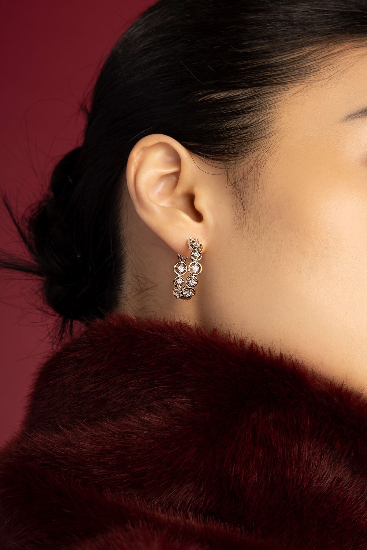 Woman wearing APM hoop earrings, a radiant whisper against crimson elegance.