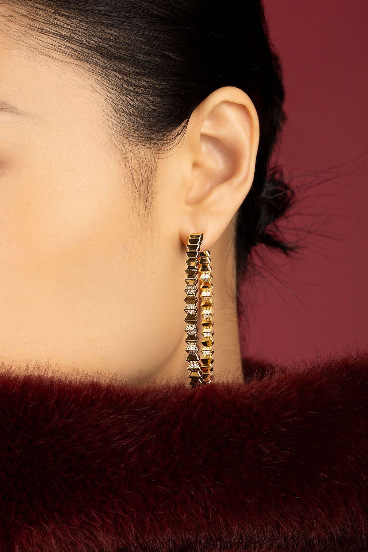 Woman wearing APM Monaco hoop earrings, bold golden edge meets quiet winter allure.