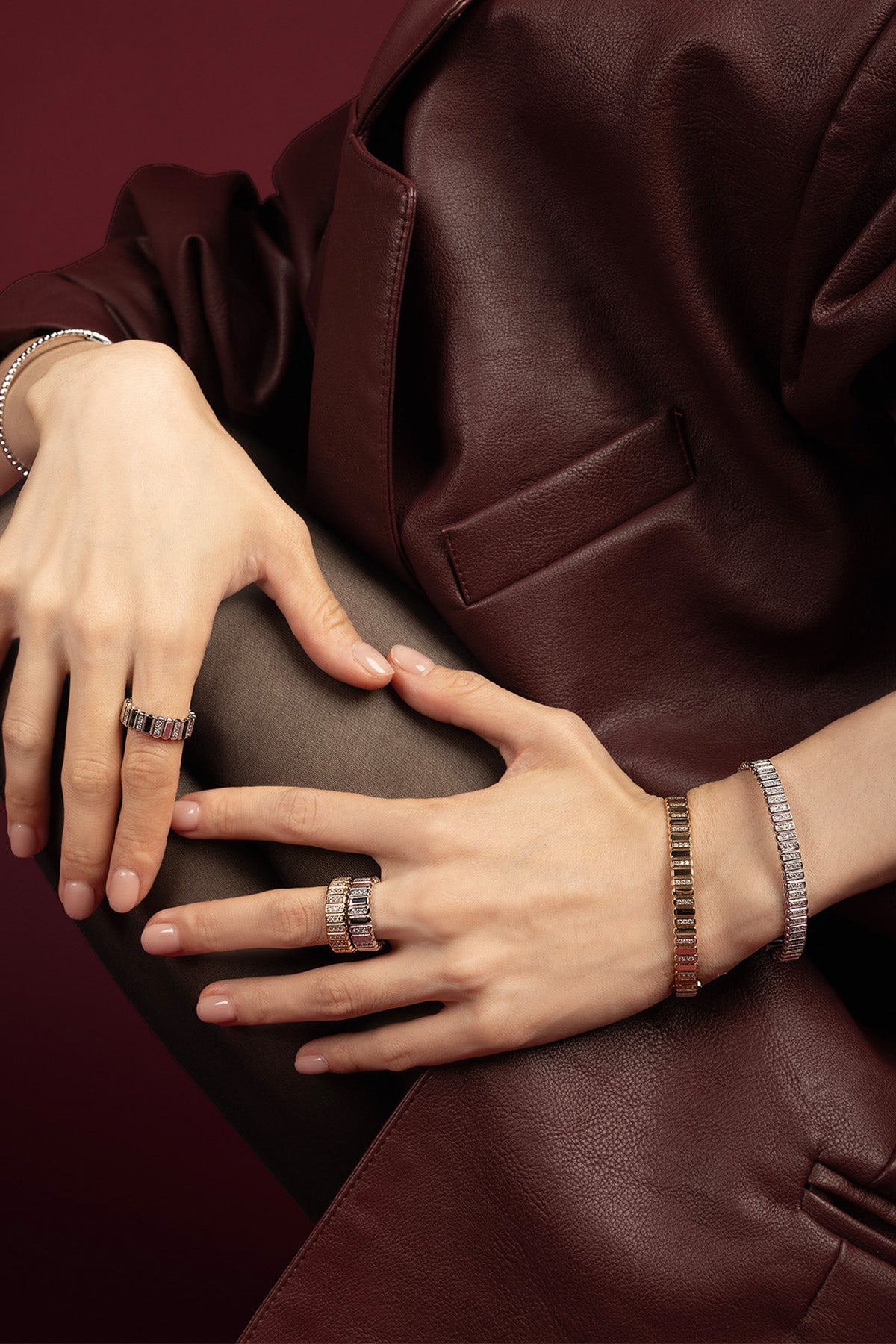Woman wearing APM Monaco rings and bracelets, a shimmering statement against rich burgundy leather.