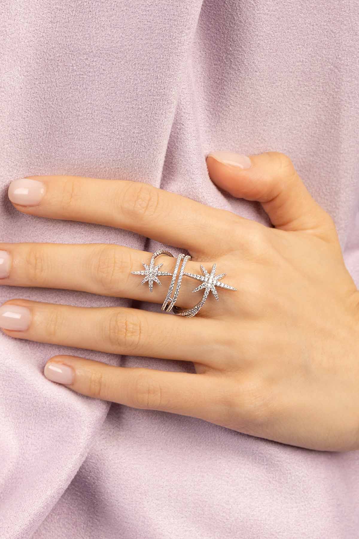 Hand wearing APM MONACO silver ring with star design on a light purple fabric background