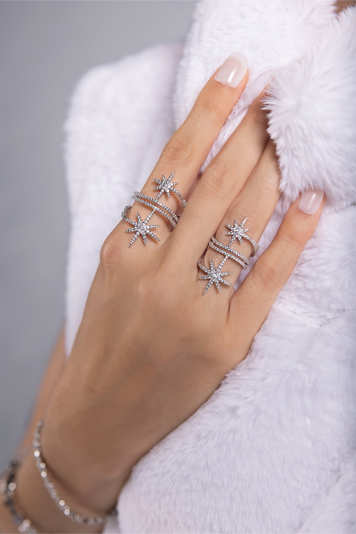 Hand wearing a silver star-shaped ring on a grey background