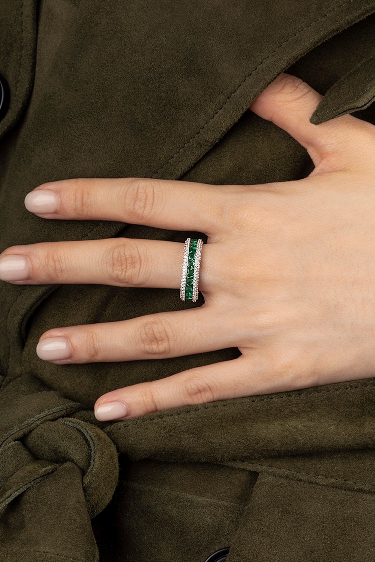 Hand wearing a ring with green stones on a brown fabric background