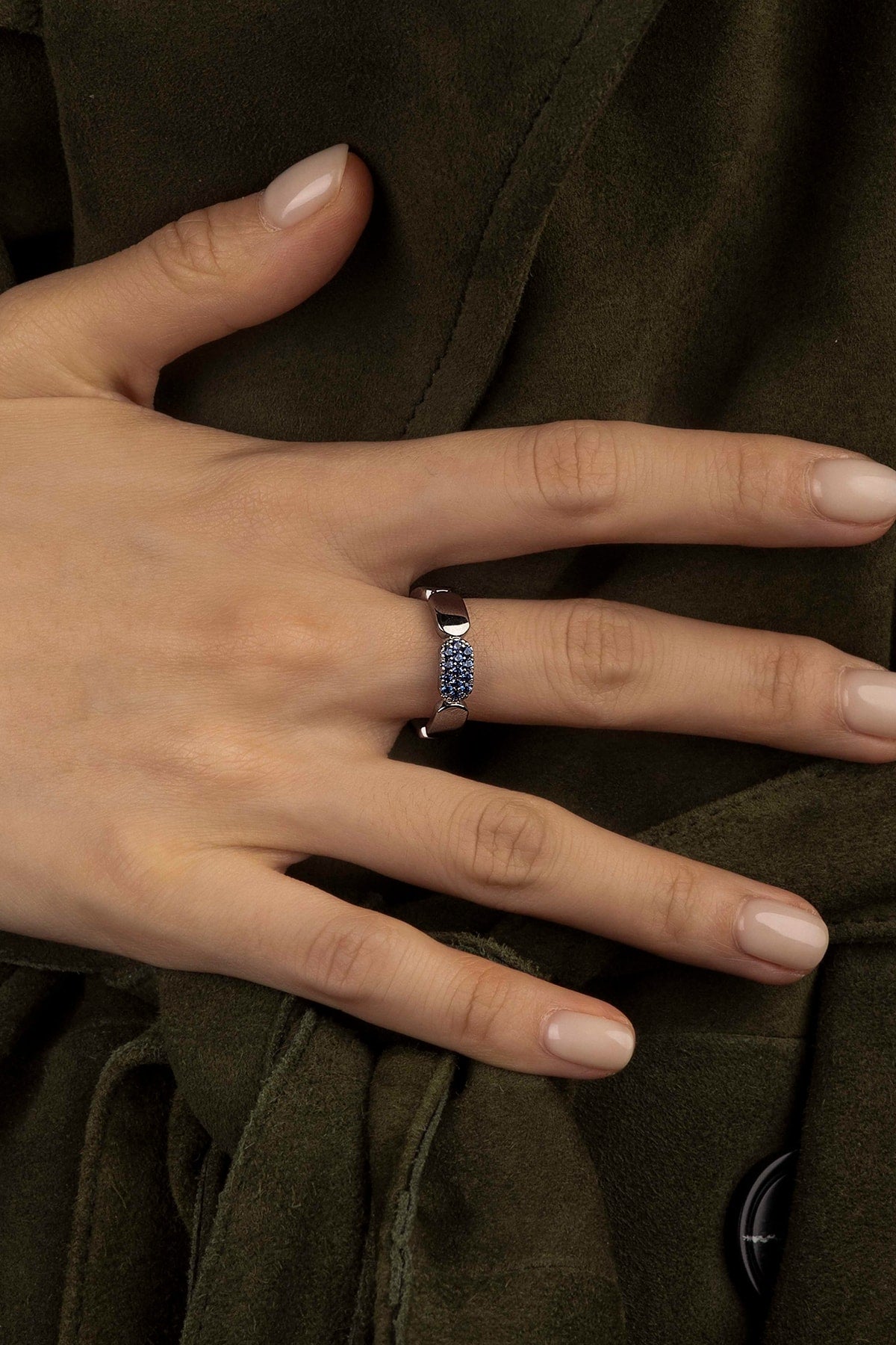 Hand wearing a ring with blue stones on a brown fabric background
