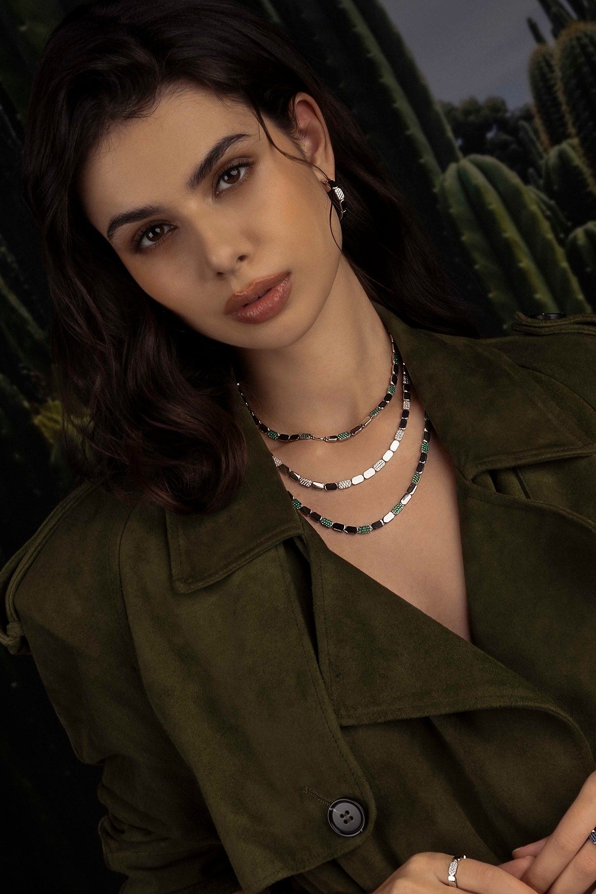 Woman wearing a green jacket and layered necklaces with cacti in the background