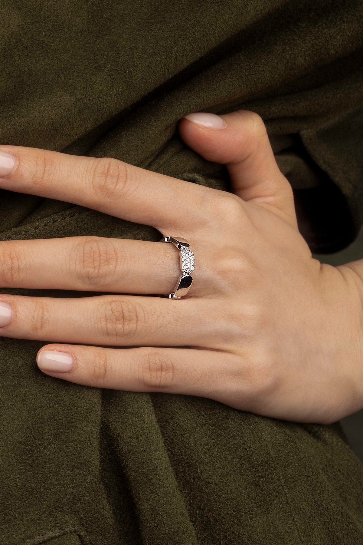 Hand wearing a silver ring on a green fabric background