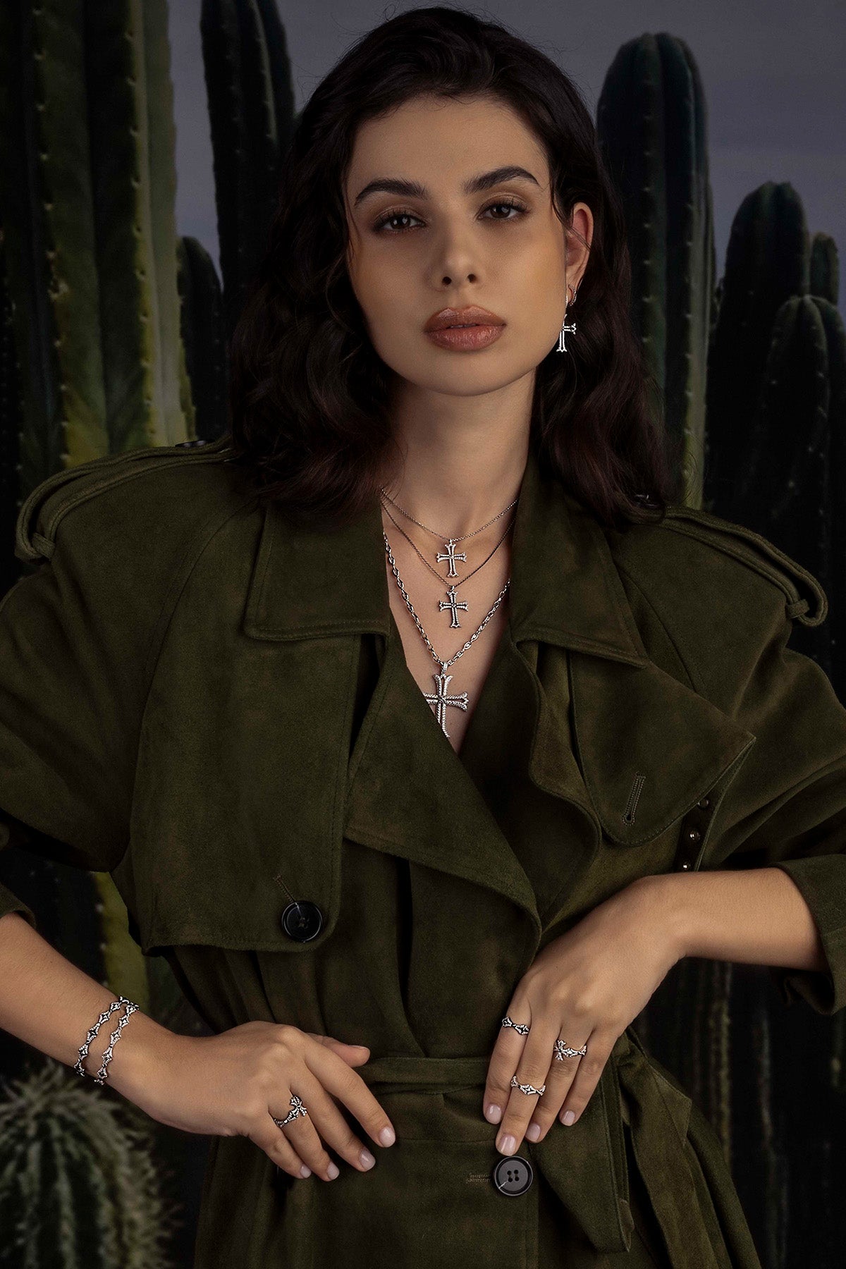 Woman wearing a green trench coat with jewelry against a cactus background