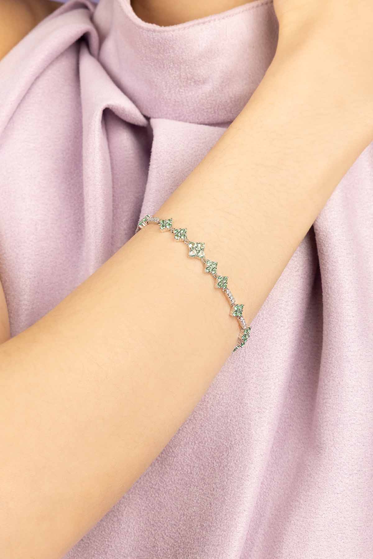 Bracelet with green stones on a person's wrist wearing a light pink top.