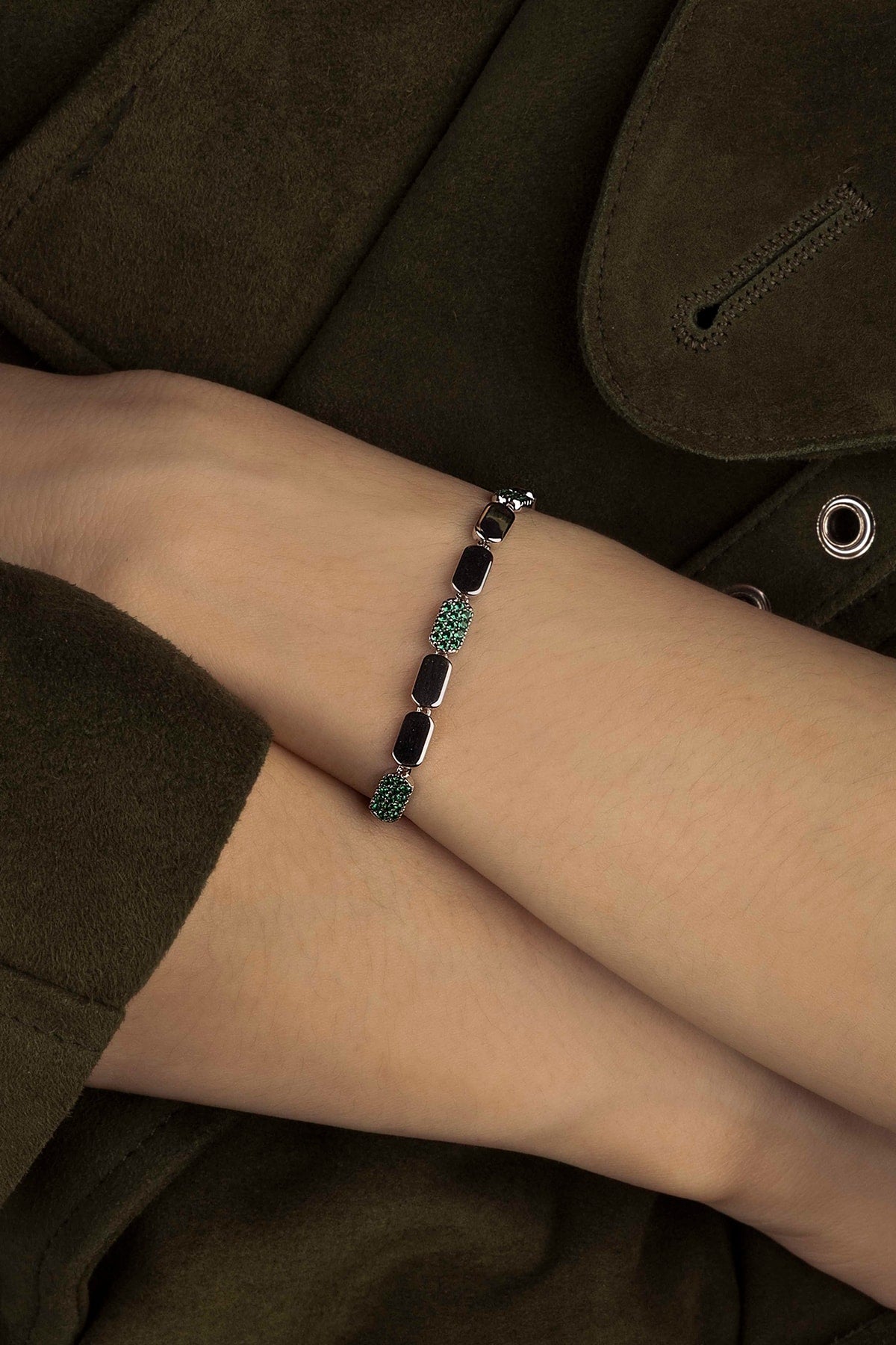 Bracelet with green stones on a wrist against a dark background