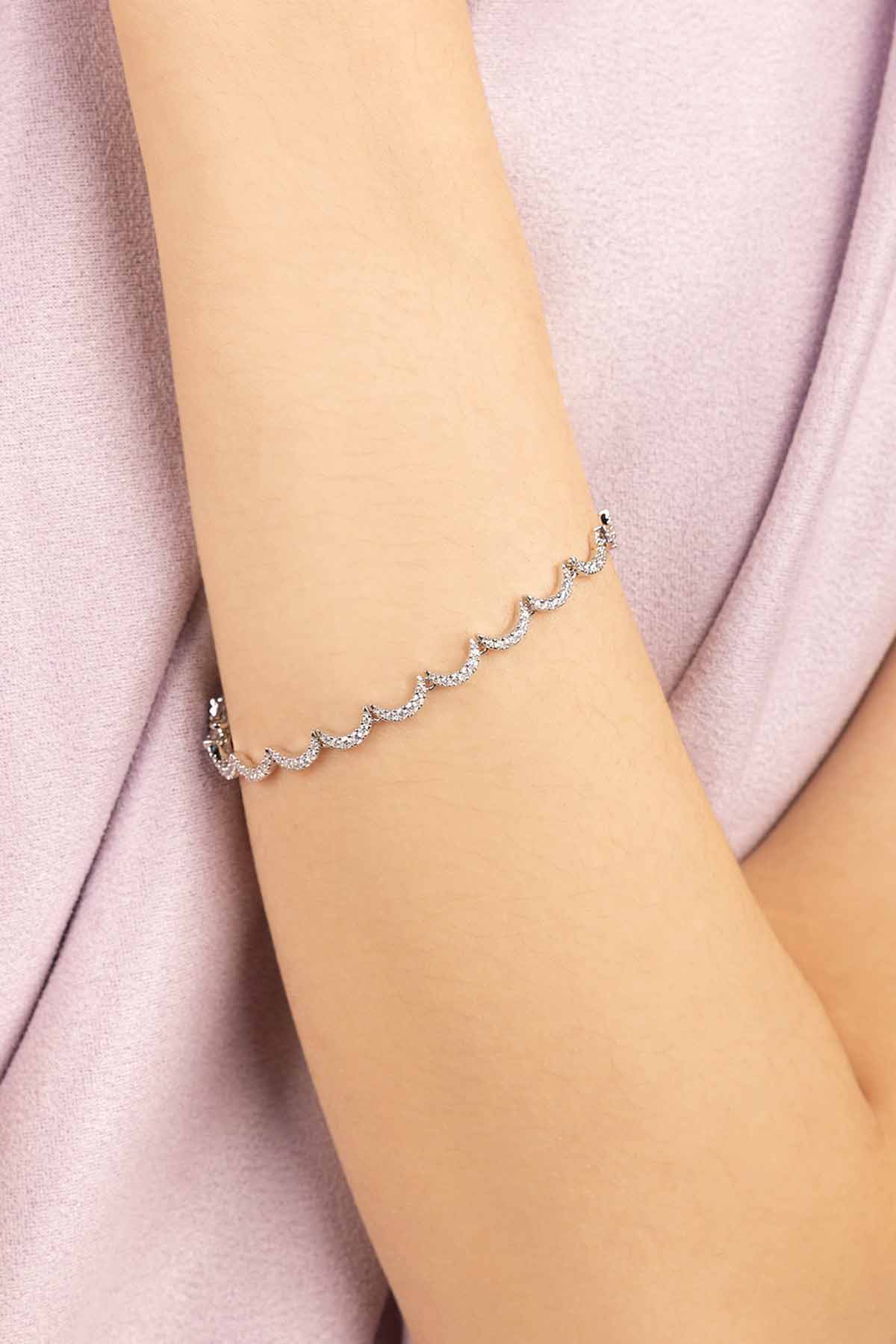 APM MONACO silver wavy bracelet on a person's wrist with a soft purple fabric background
