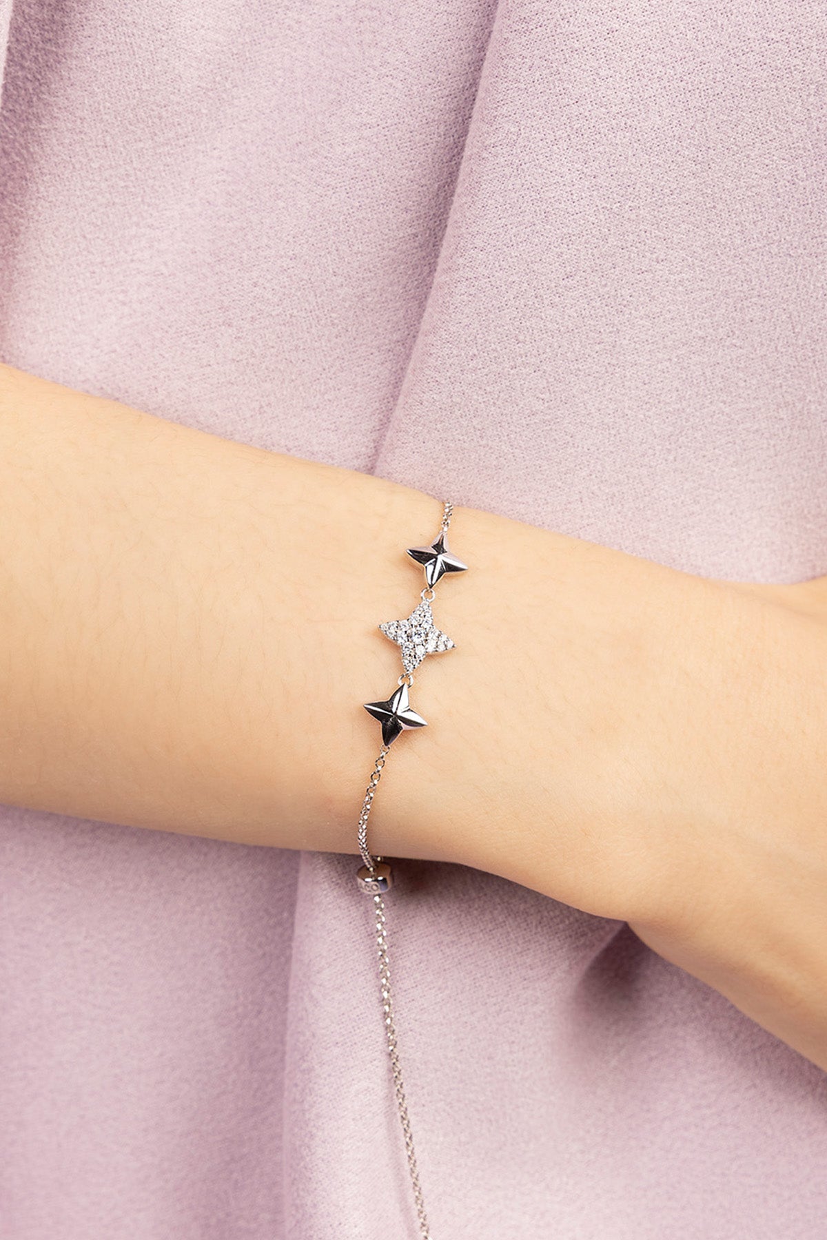 Silver bracelet with star-shaped charms on a wrist against a pink fabric background