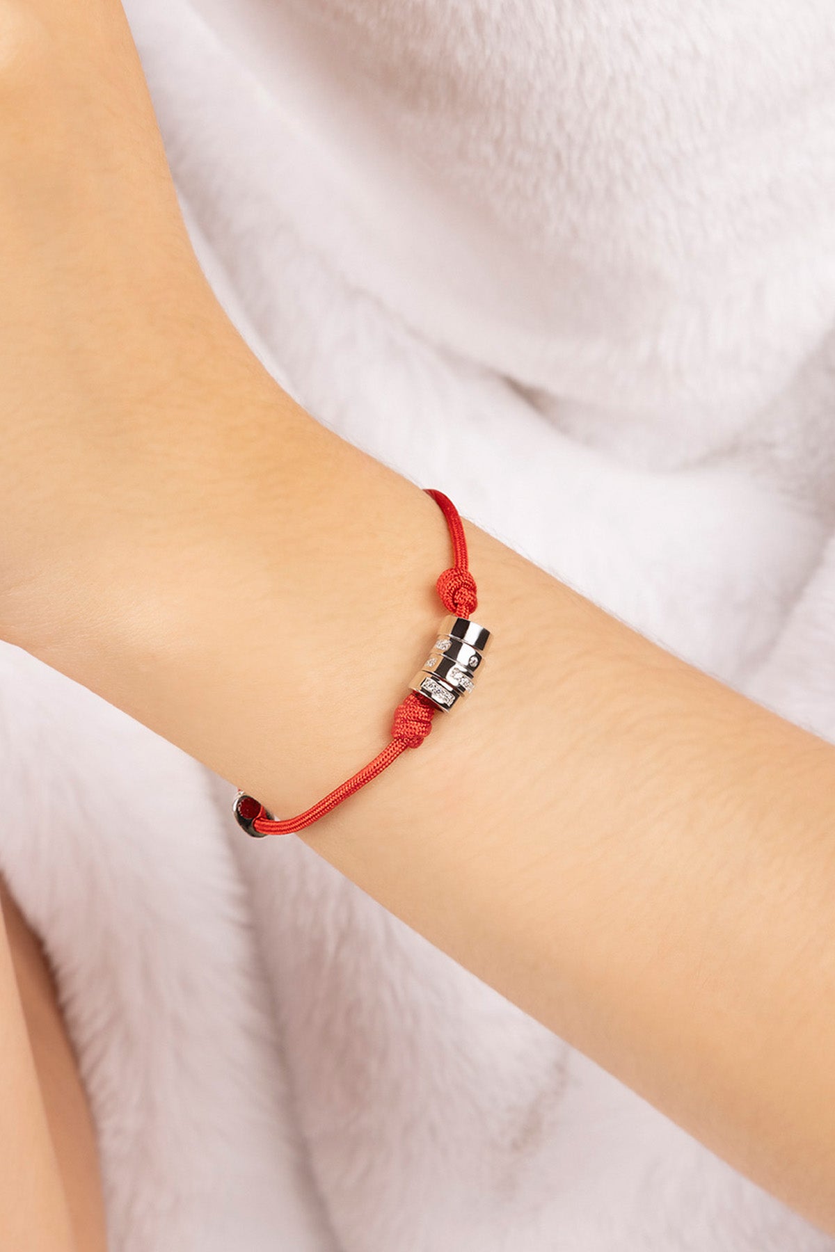 Red string bracelet with a silver charm on a wrist against a white background