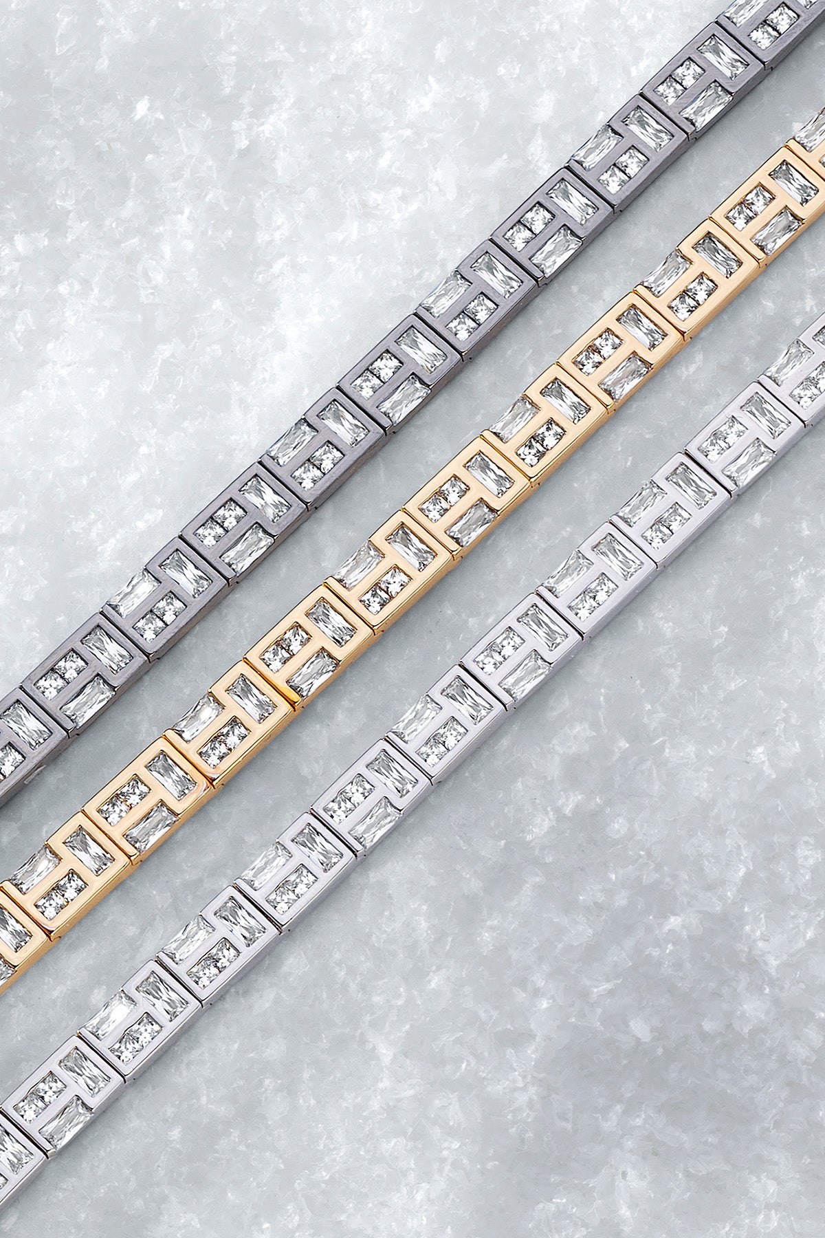 Three labyrinth bracelets in yellow gold, silver, and dark gray on a light iced background.