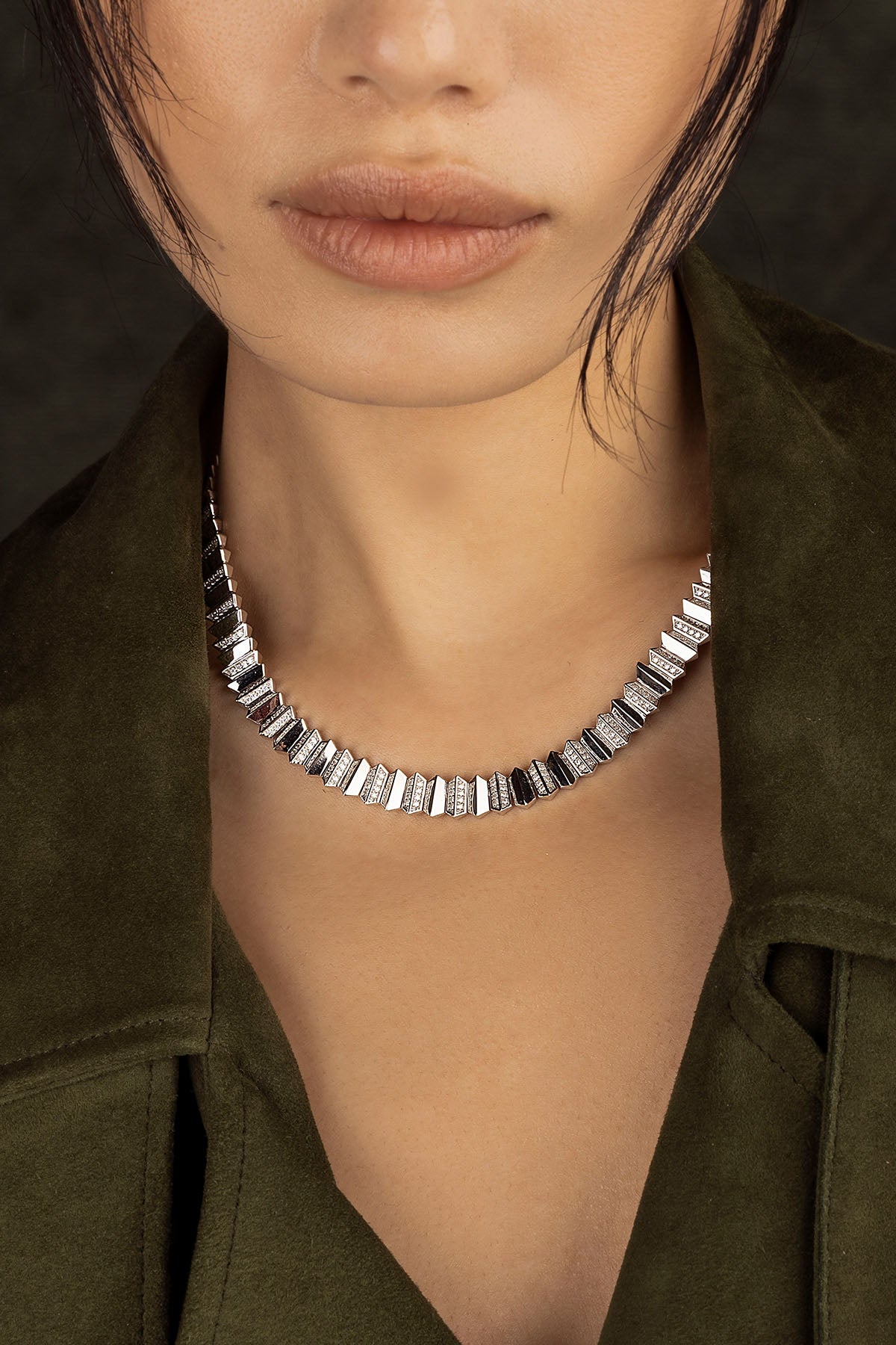 Close-up of a model wearing a silver necklace with a dark background