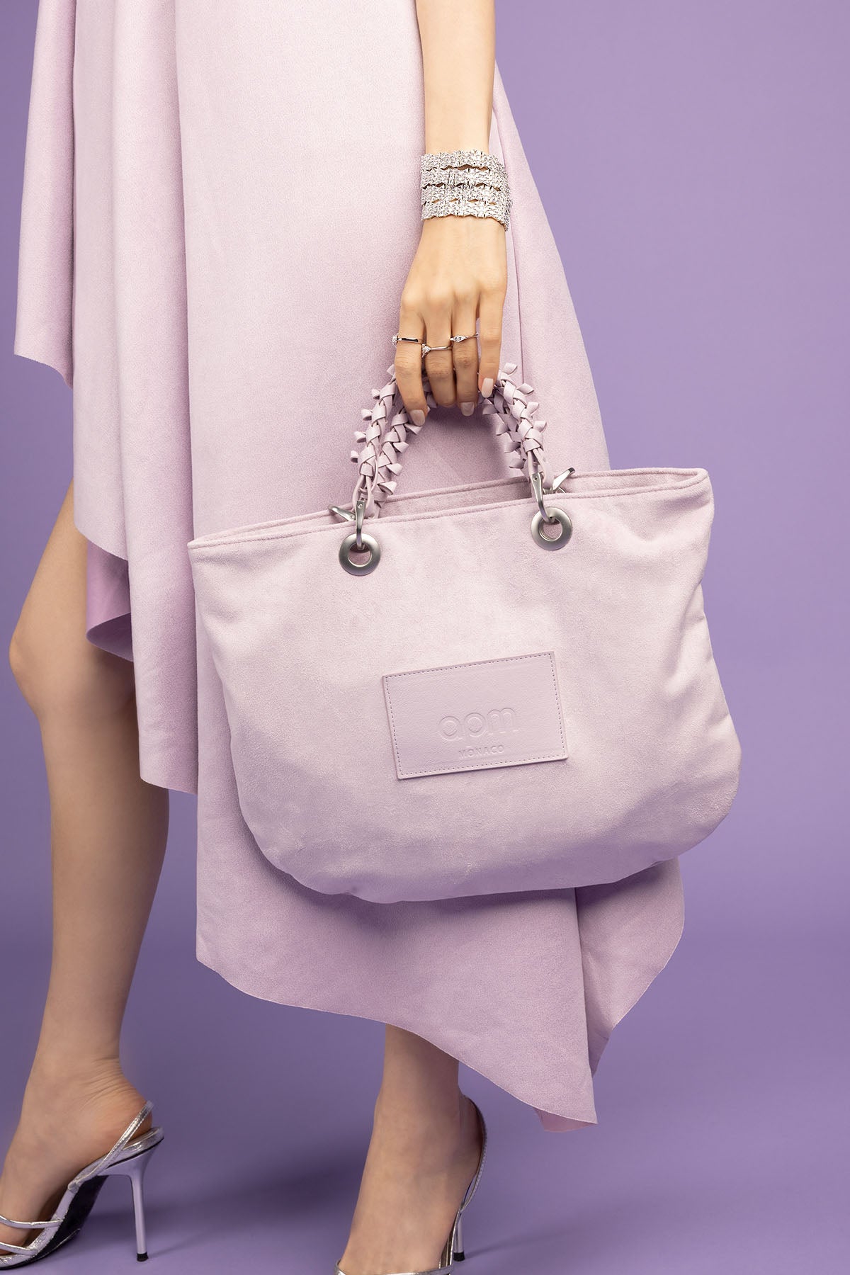 Person holding a light purple handbag with a visible APM Monaco logo against a purple background
