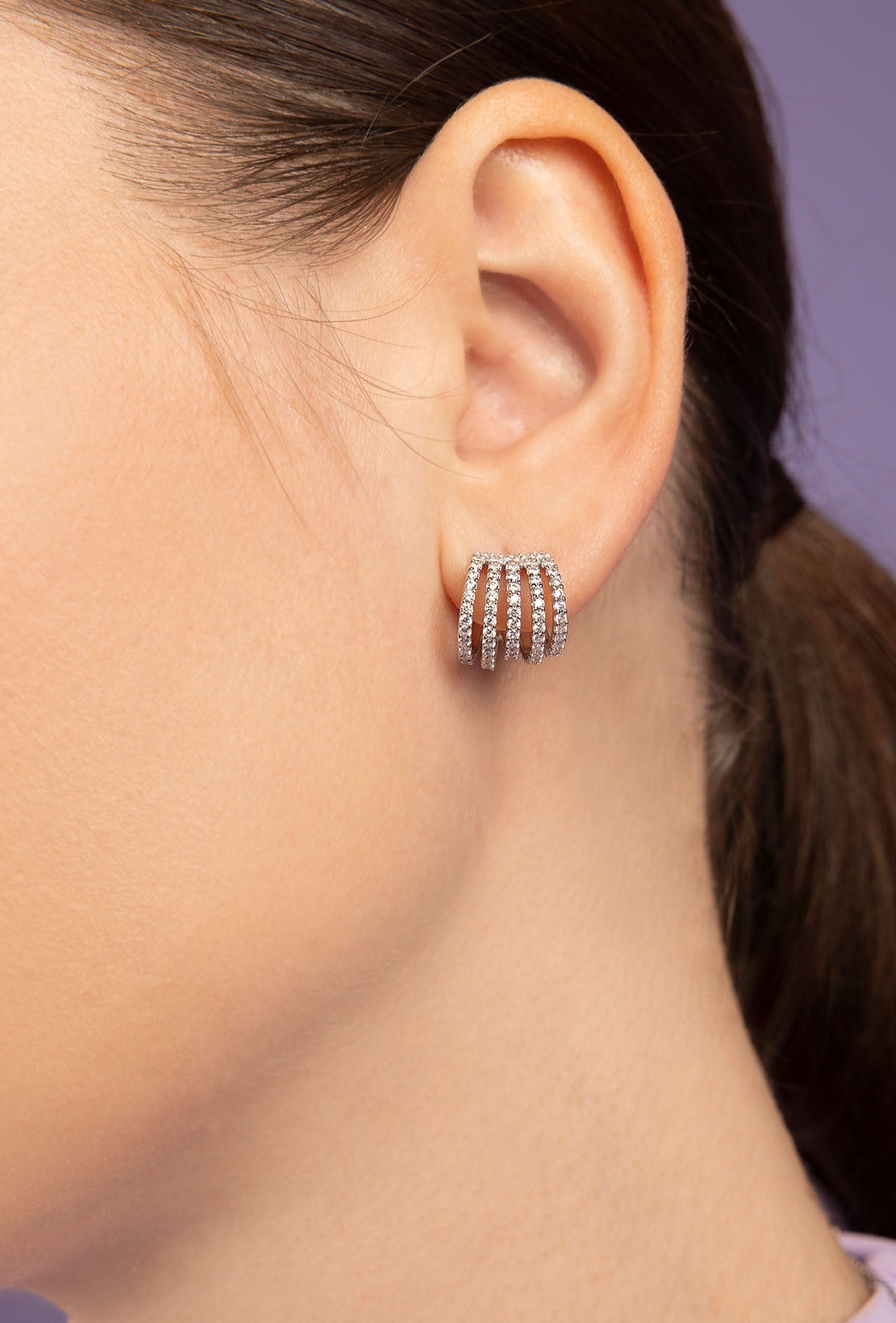 Close-up of an ear wearing APM MOANCO silver hoop earring with a purple blurred background