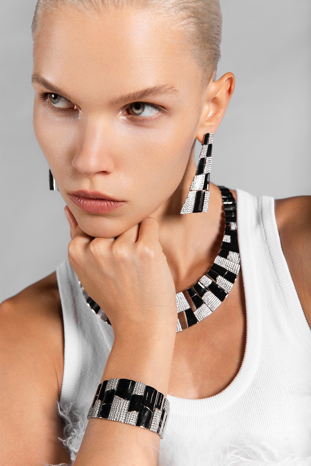 Woman wearing black and white patterned earrings and bracelet against a gray background
