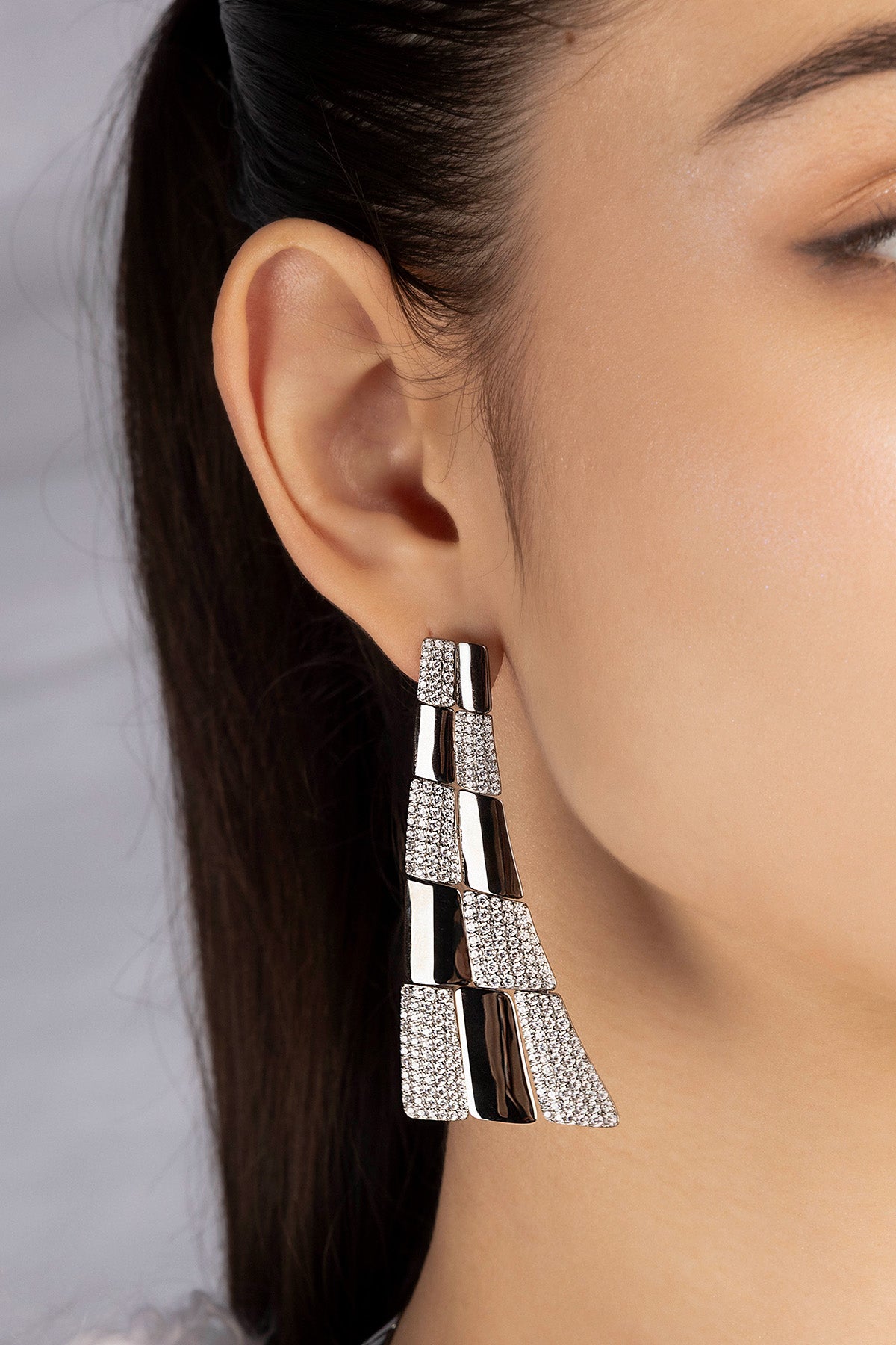 Close-up of a silver earring worn by a model with a neutral background