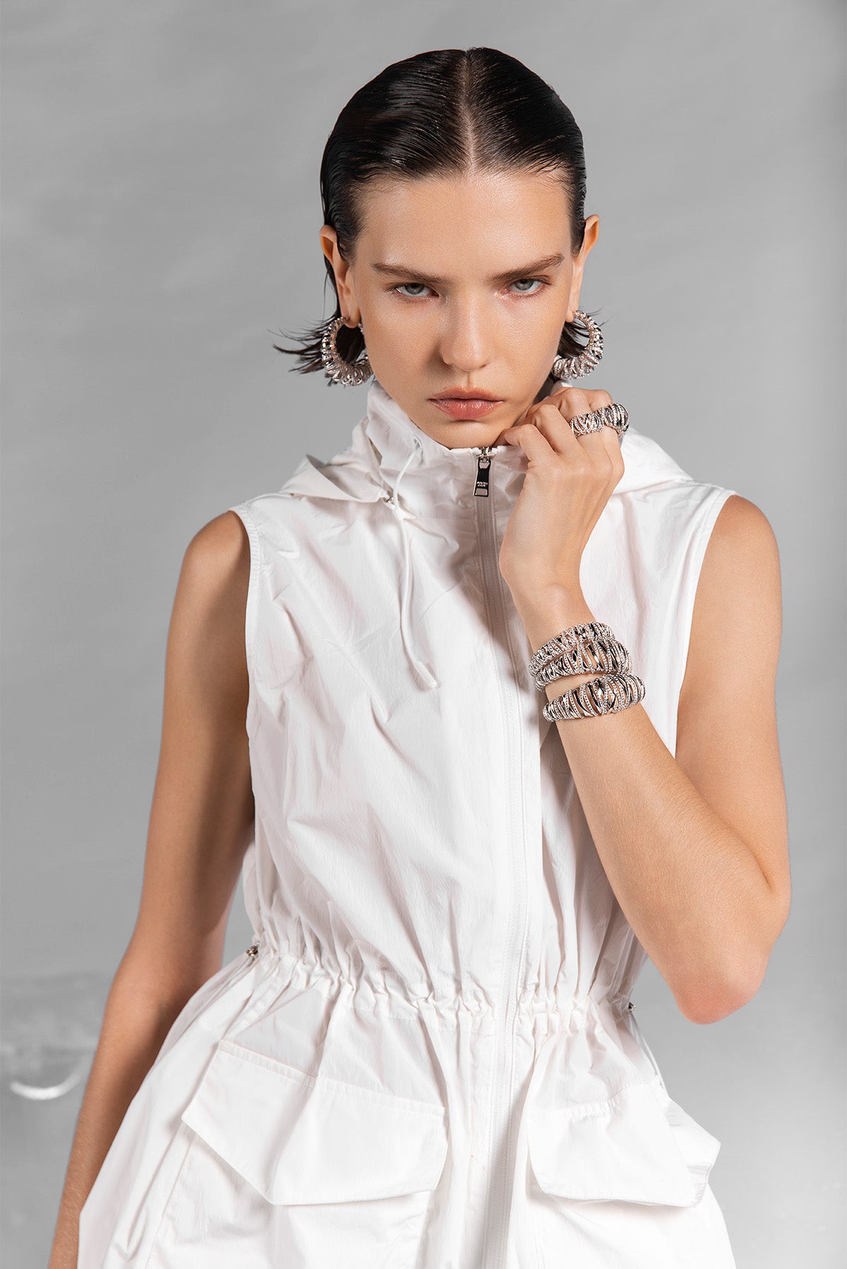 Woman wearing a white sleeveless dress with APM MONACO jewelry on a gray background