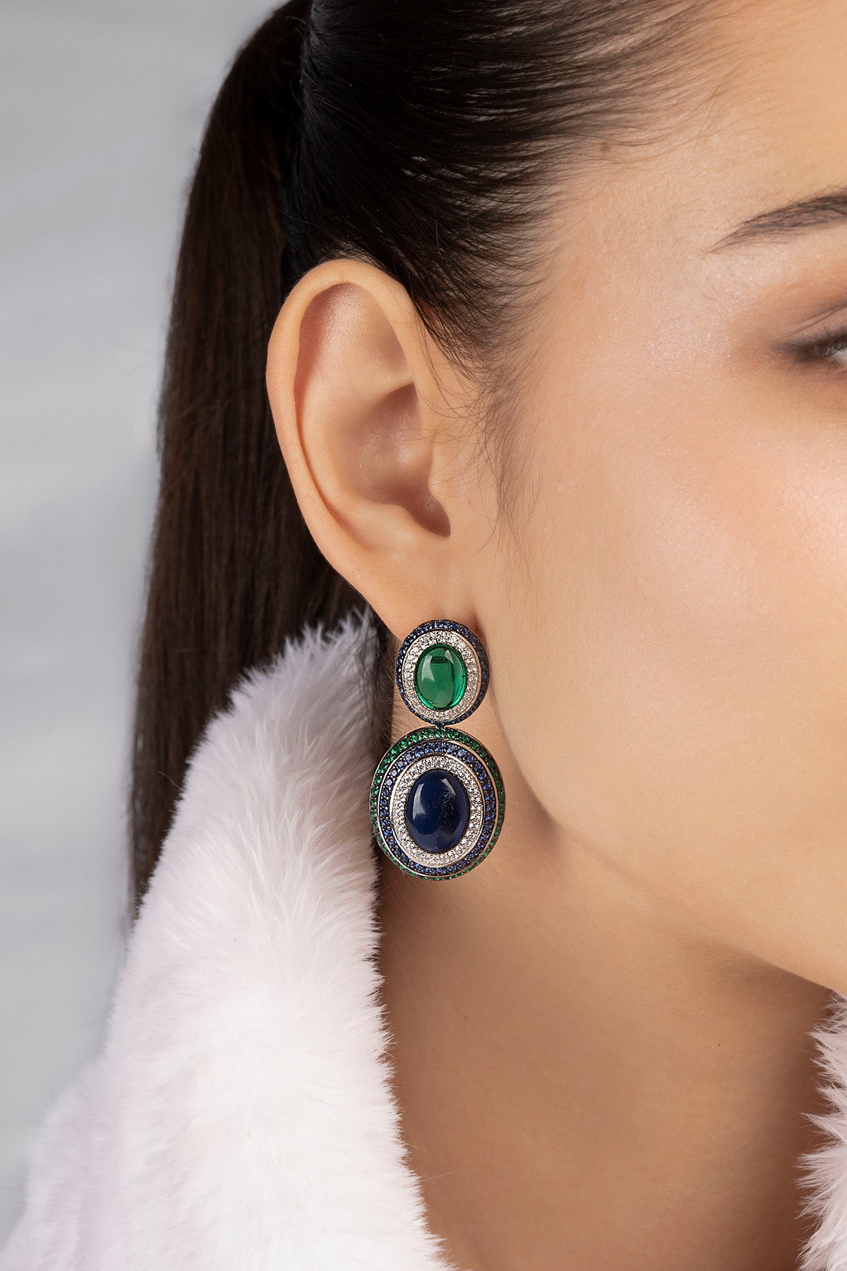 Close-up of a woman wearing a pair of earrings with green and blue gemstones.