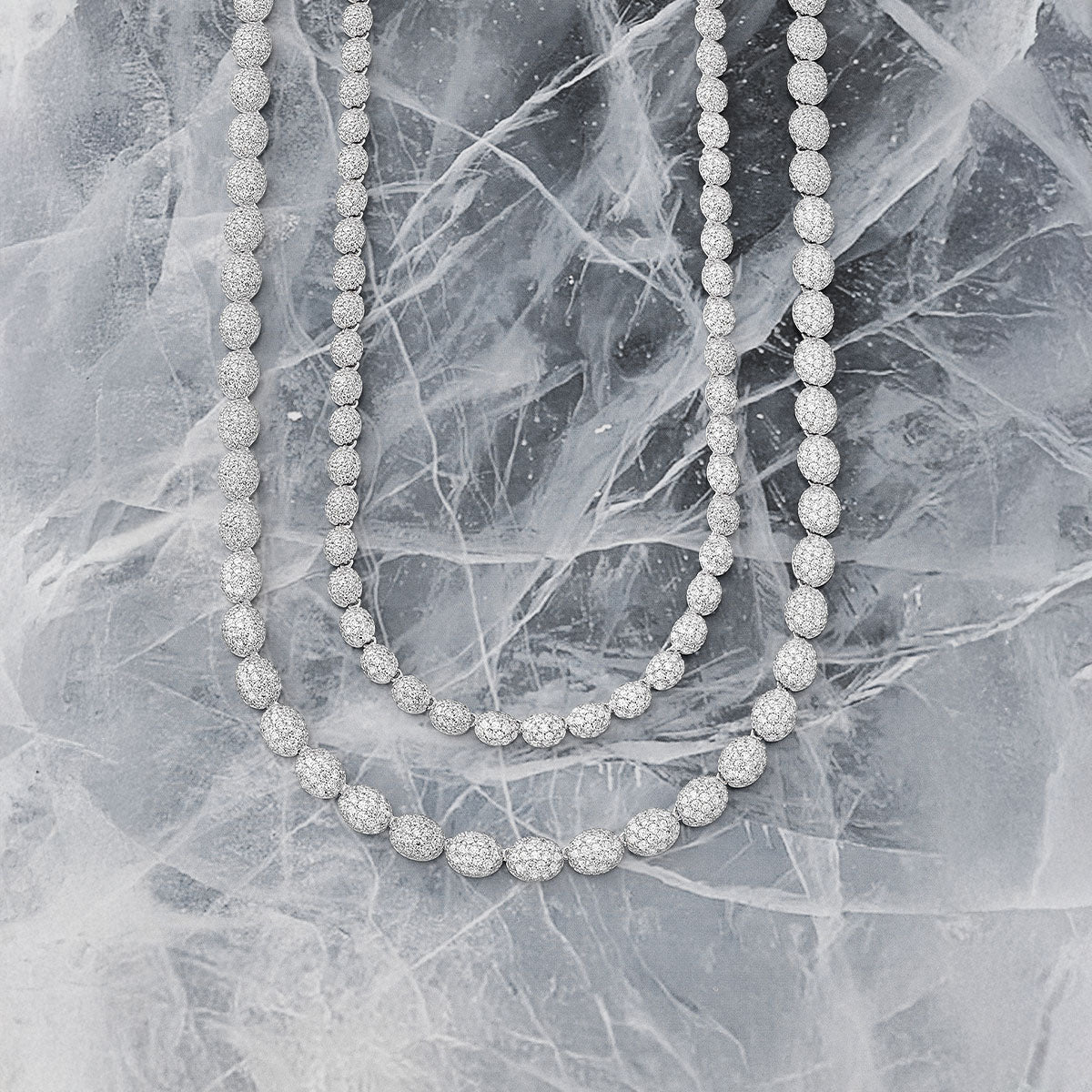 Two APM MONACO silver necklaces on a textured gray surface