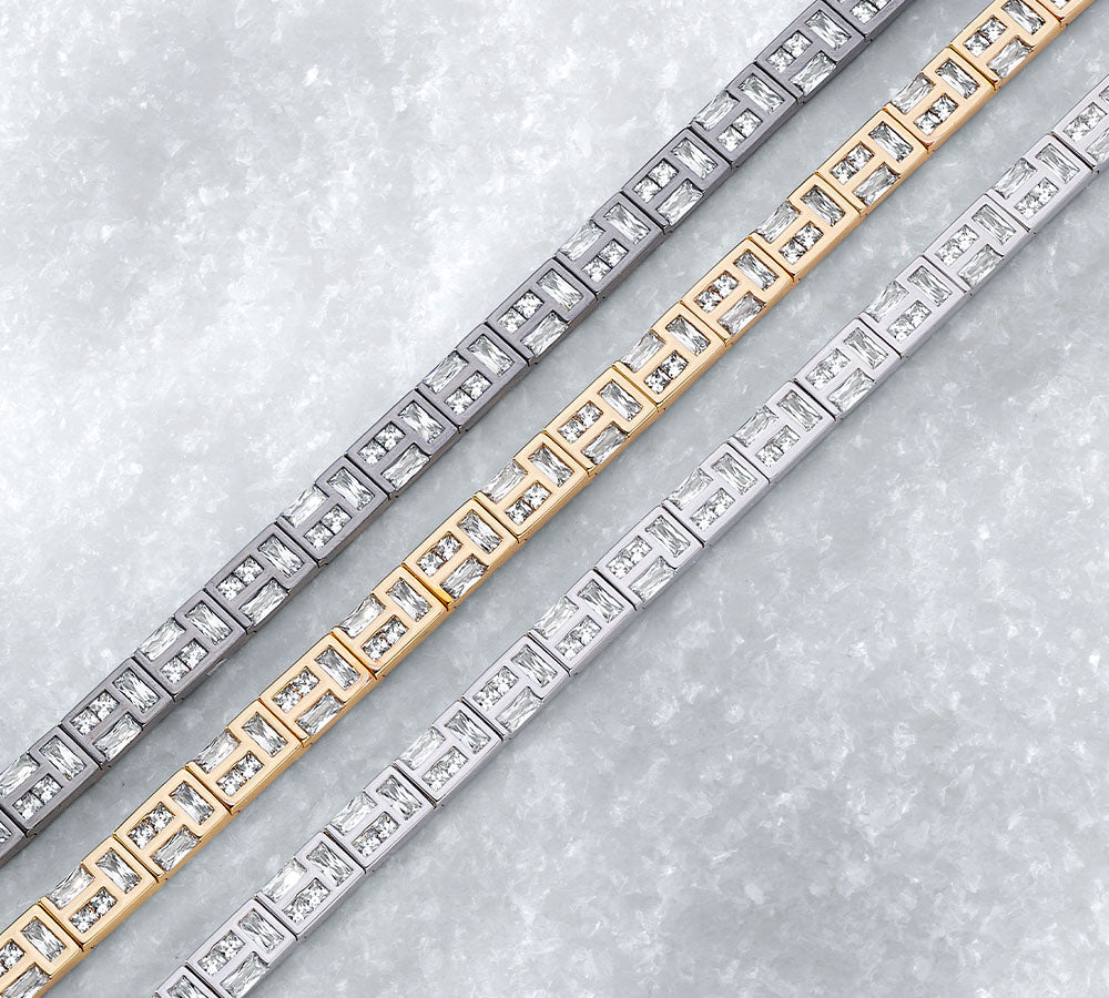 Three APM MONACO hiver bracelets in yellow gold, silver, and dark grey on a light gray background