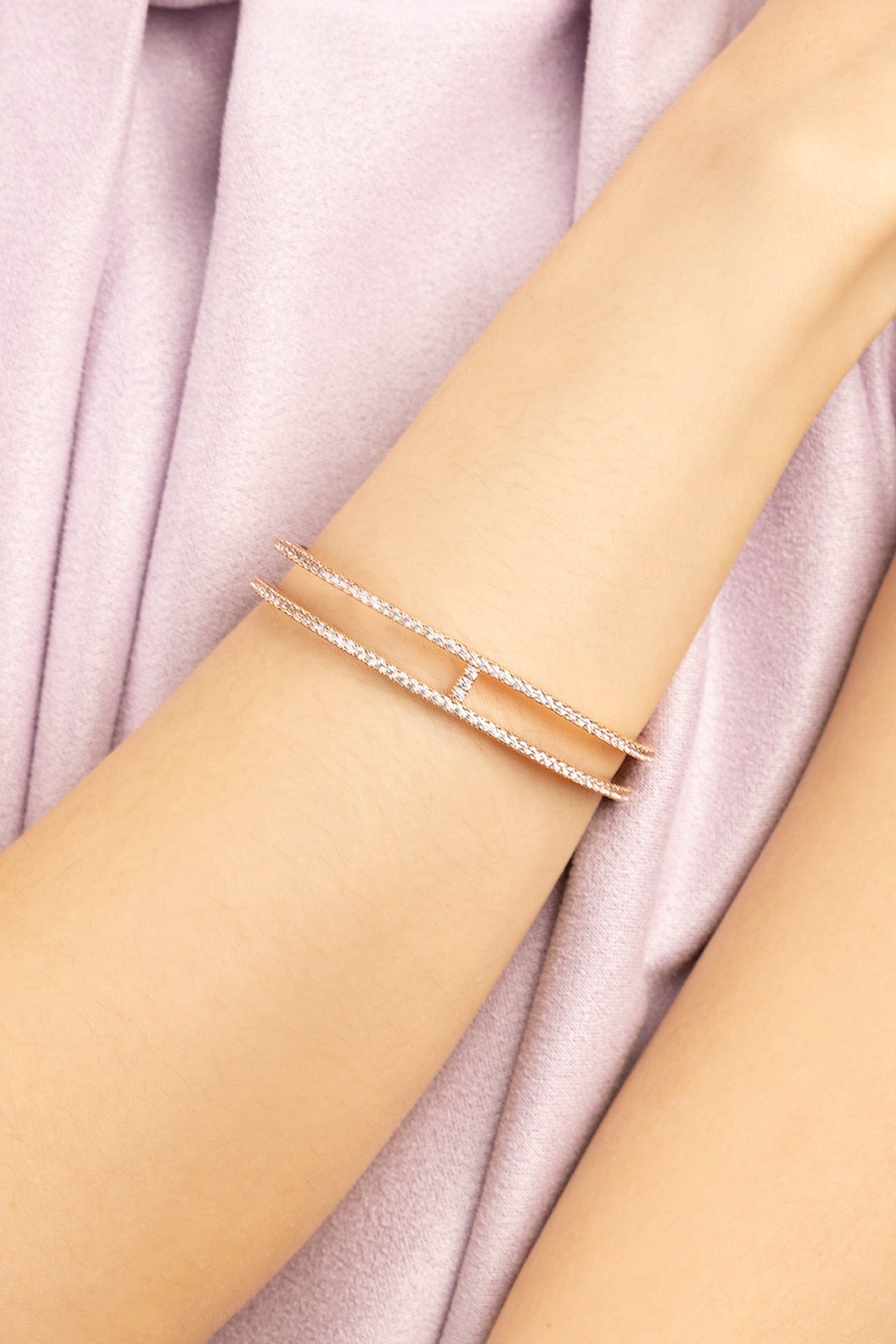 APM MONACO rose gold double line pave cuff on a person's wrist with a soft purple fabric background