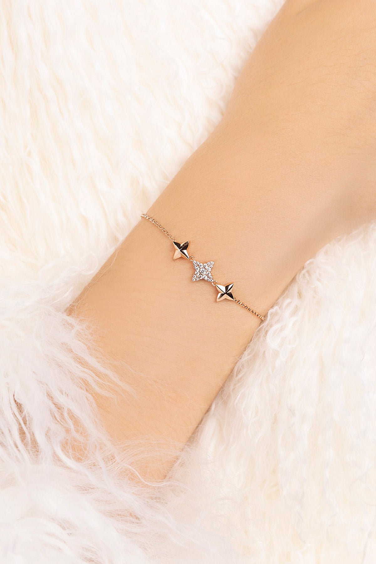 Rose gold bracelet with star-shaped charms on a wrist against a soft white background