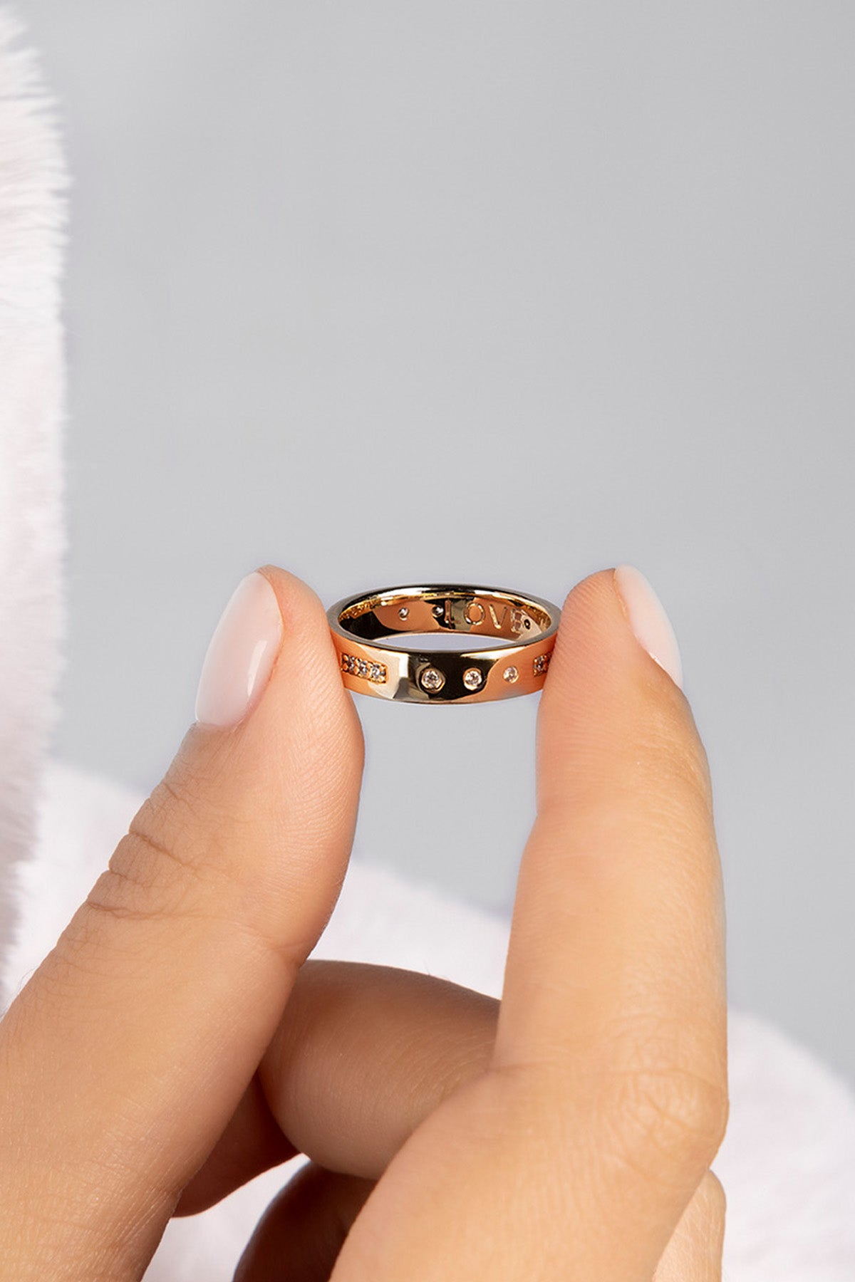 Rose gold ring with small stones held between two fingers against a light gray background