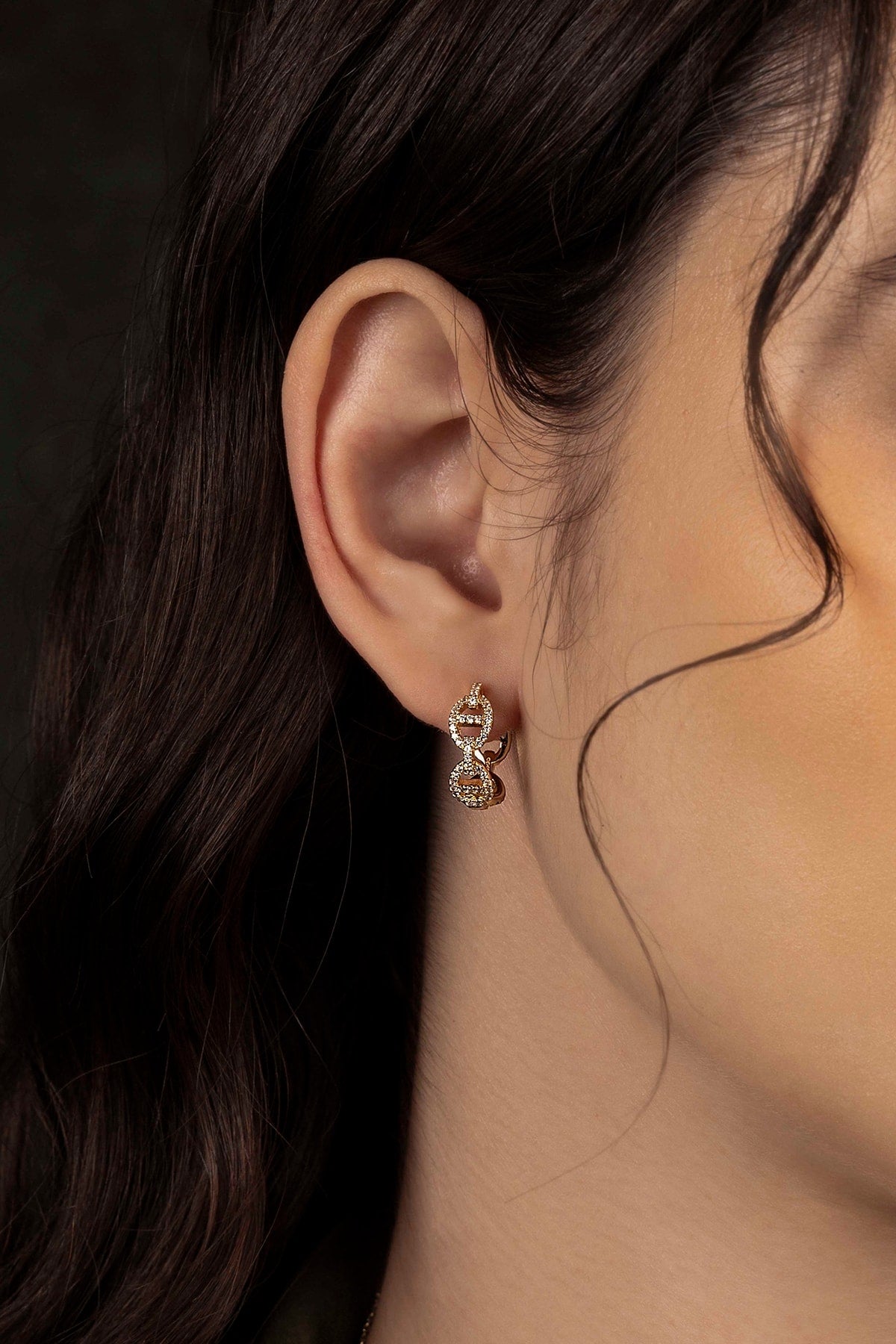 Close-up of an ear wearing a gold earring with a dark background
