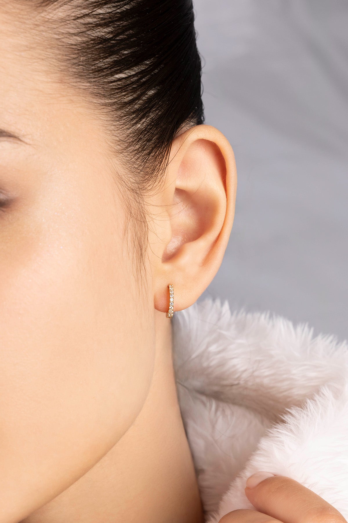 Close-up of a person wearing a huggie earring from APM MONACO with a soft gray background