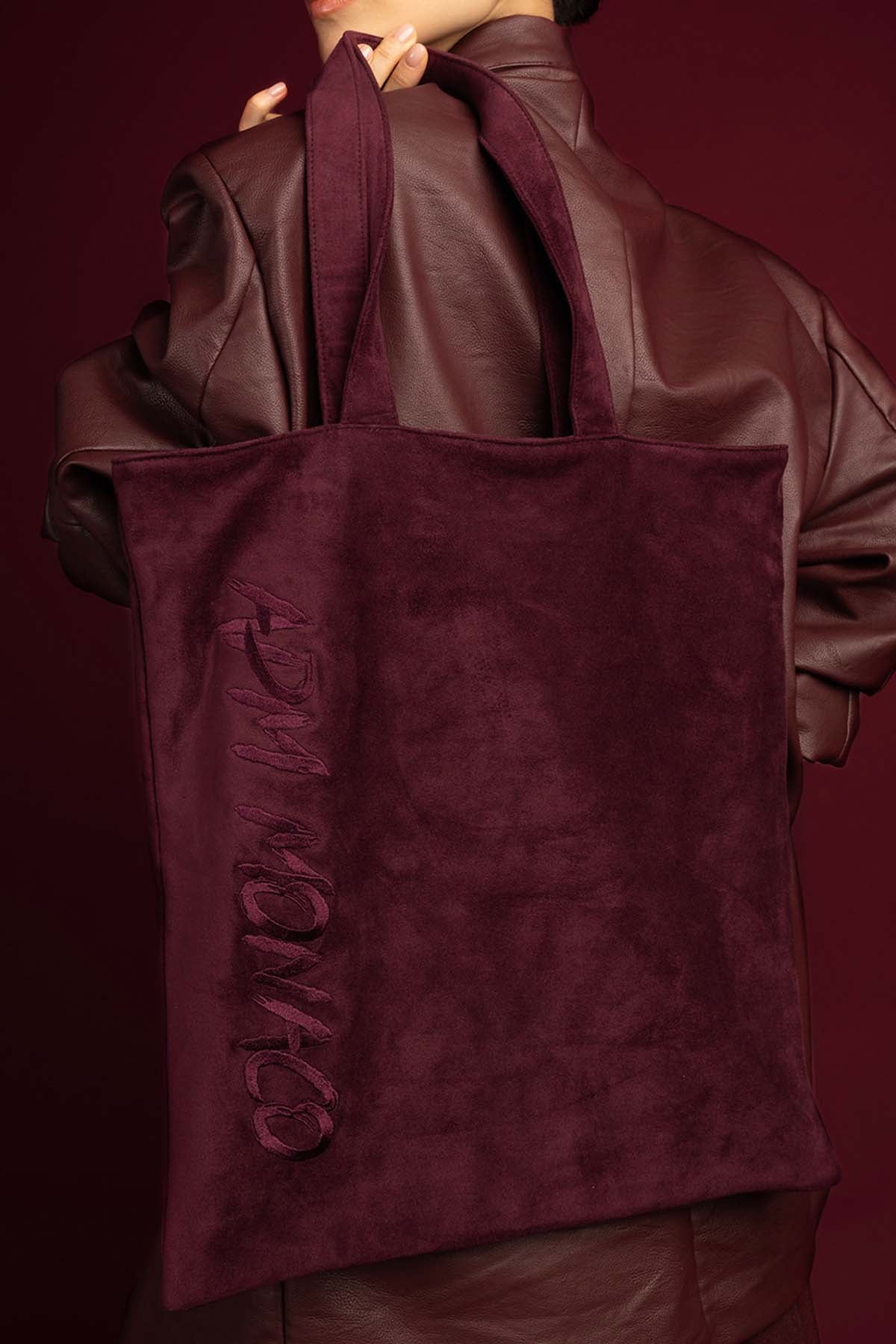 Woman carrying APM Monaco tote bag, deep burgundy softness with an effortless signature.