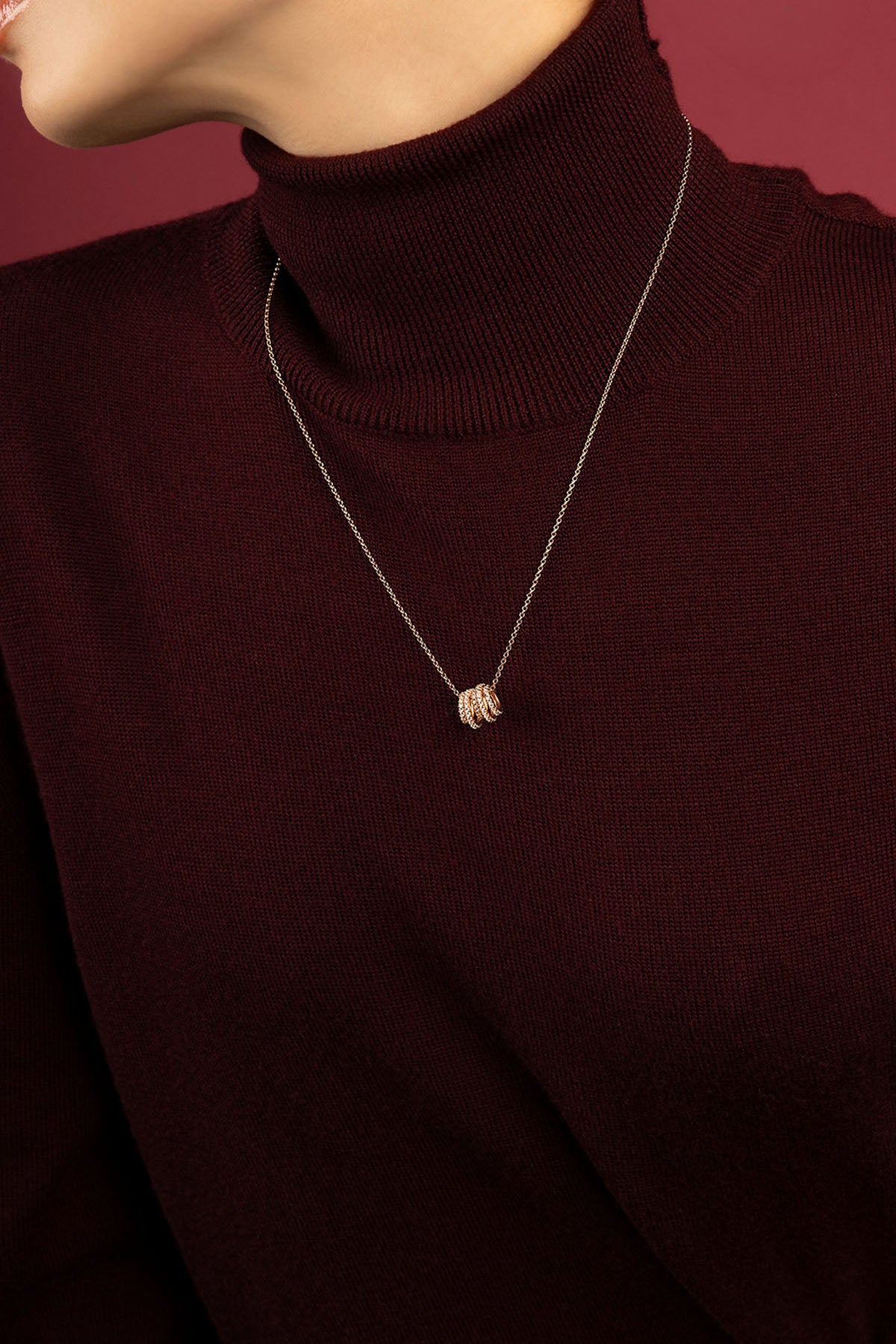 Woman wearing APM necklace, delicate charms resting on rich burgundy knit.