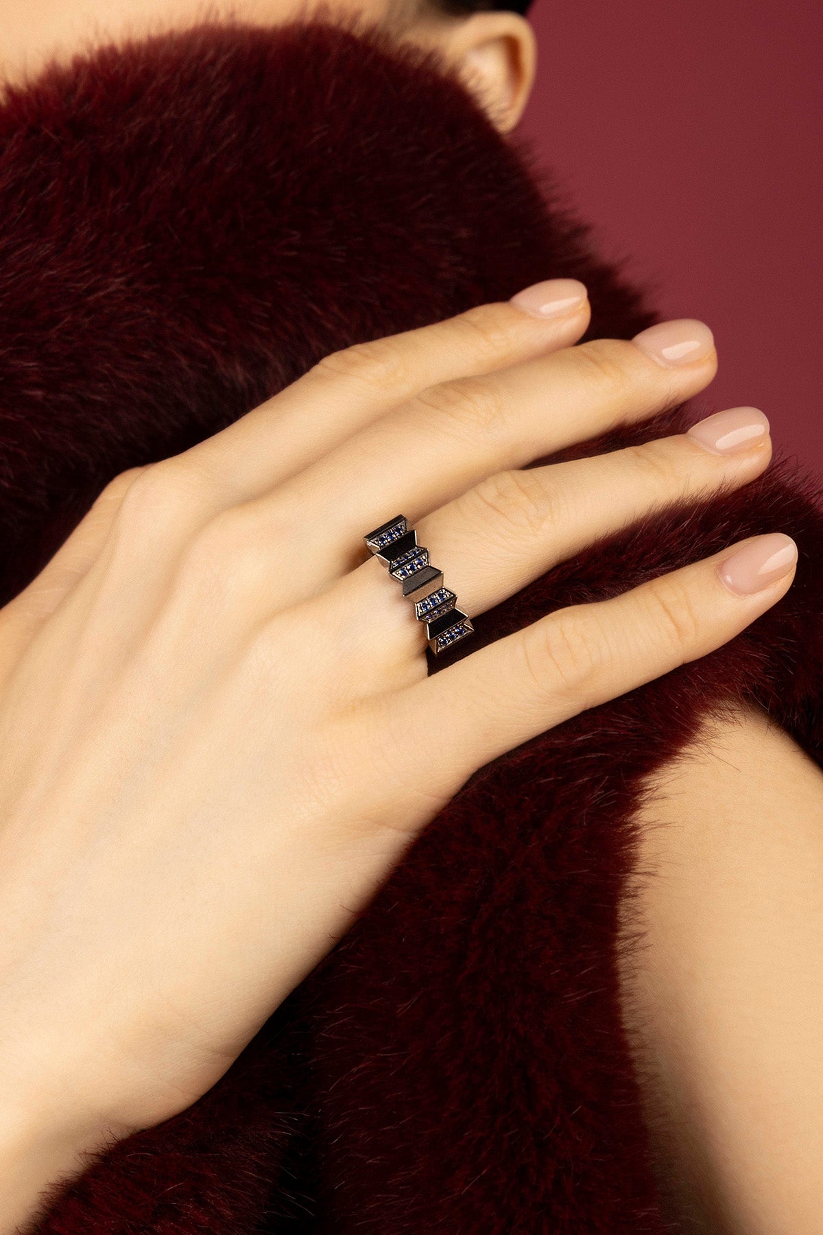Woman wearing APM ring, a bold zigzag rhythm against plush burgundy elegance.