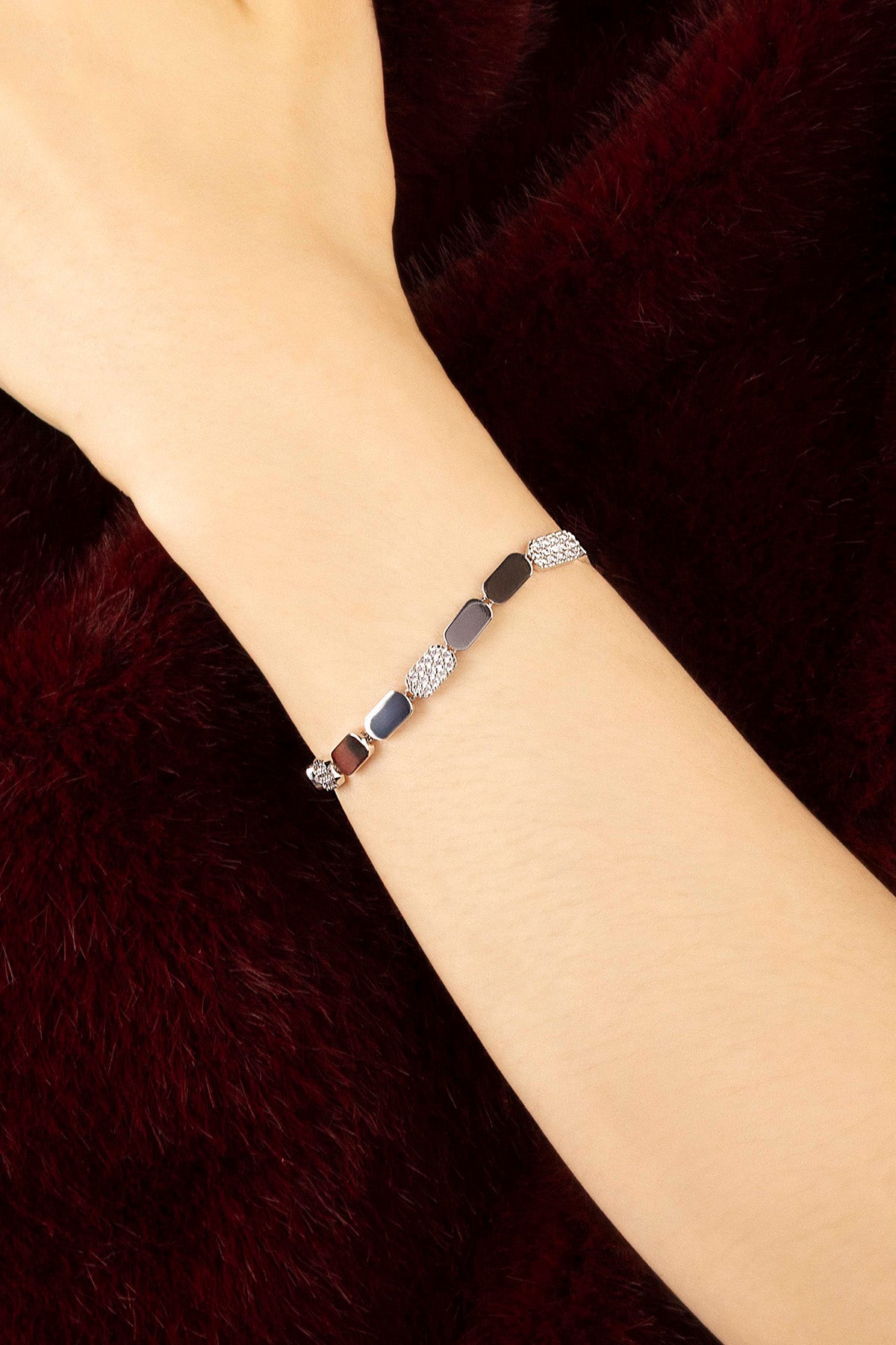 Woman wearing APM Monaco bracelet, delicate links in soft colors, quiet elegance.