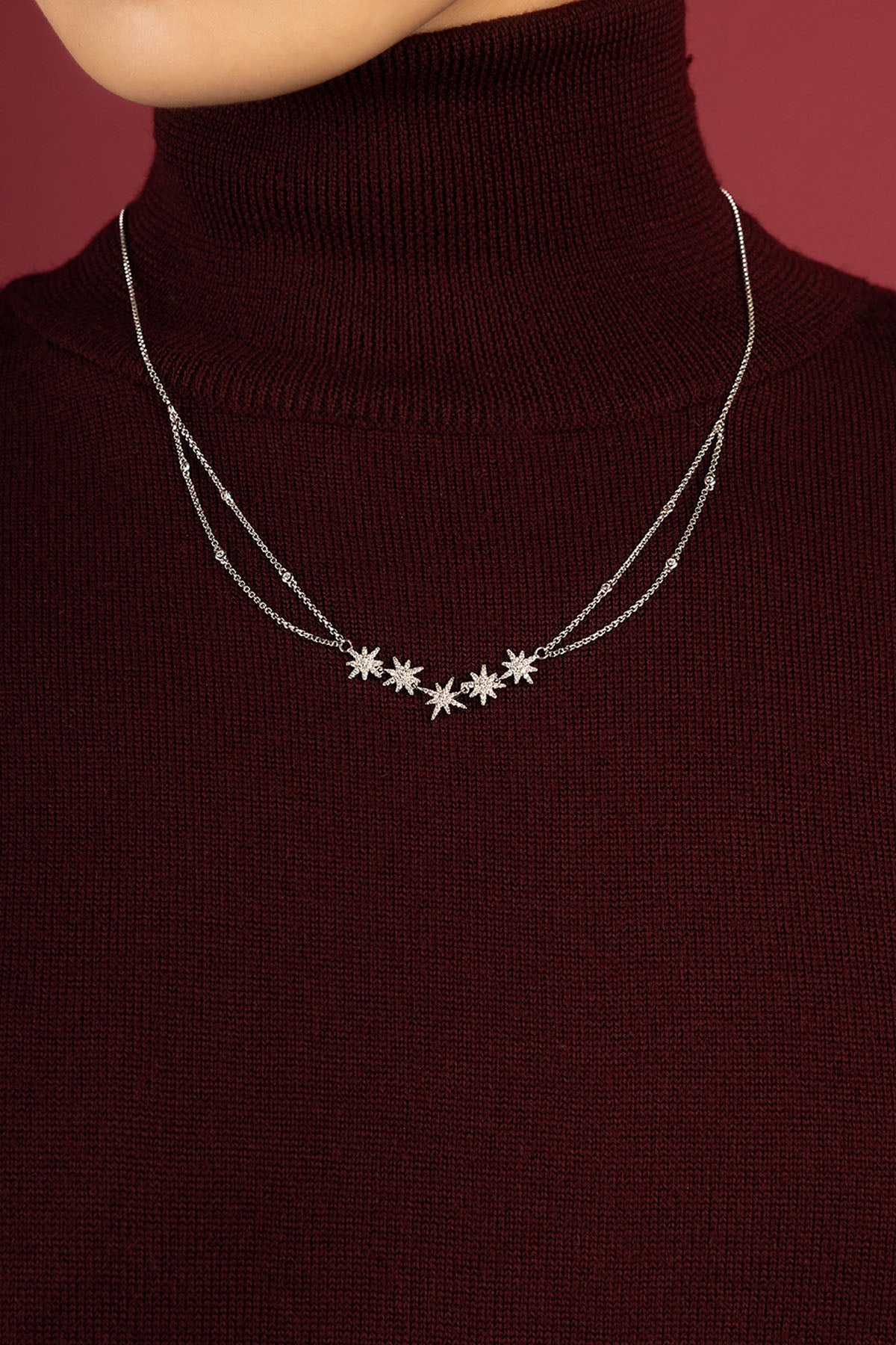 Woman wearing APM Météorites Necklace, a constellation of stars glowing softly on burgundy.