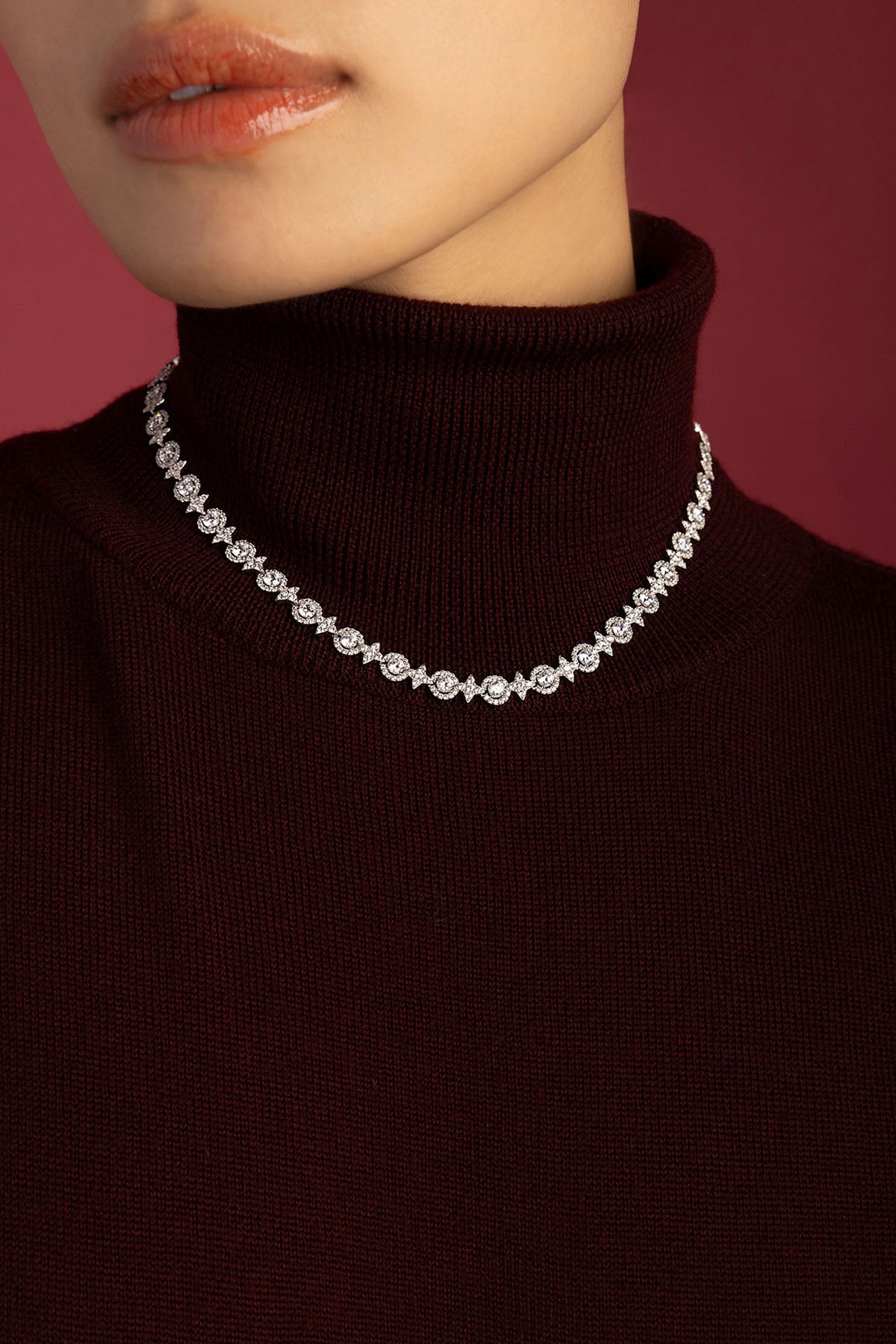 Woman wearing APM Monaco necklace, a radiant sparkle against cozy burgundy elegance.