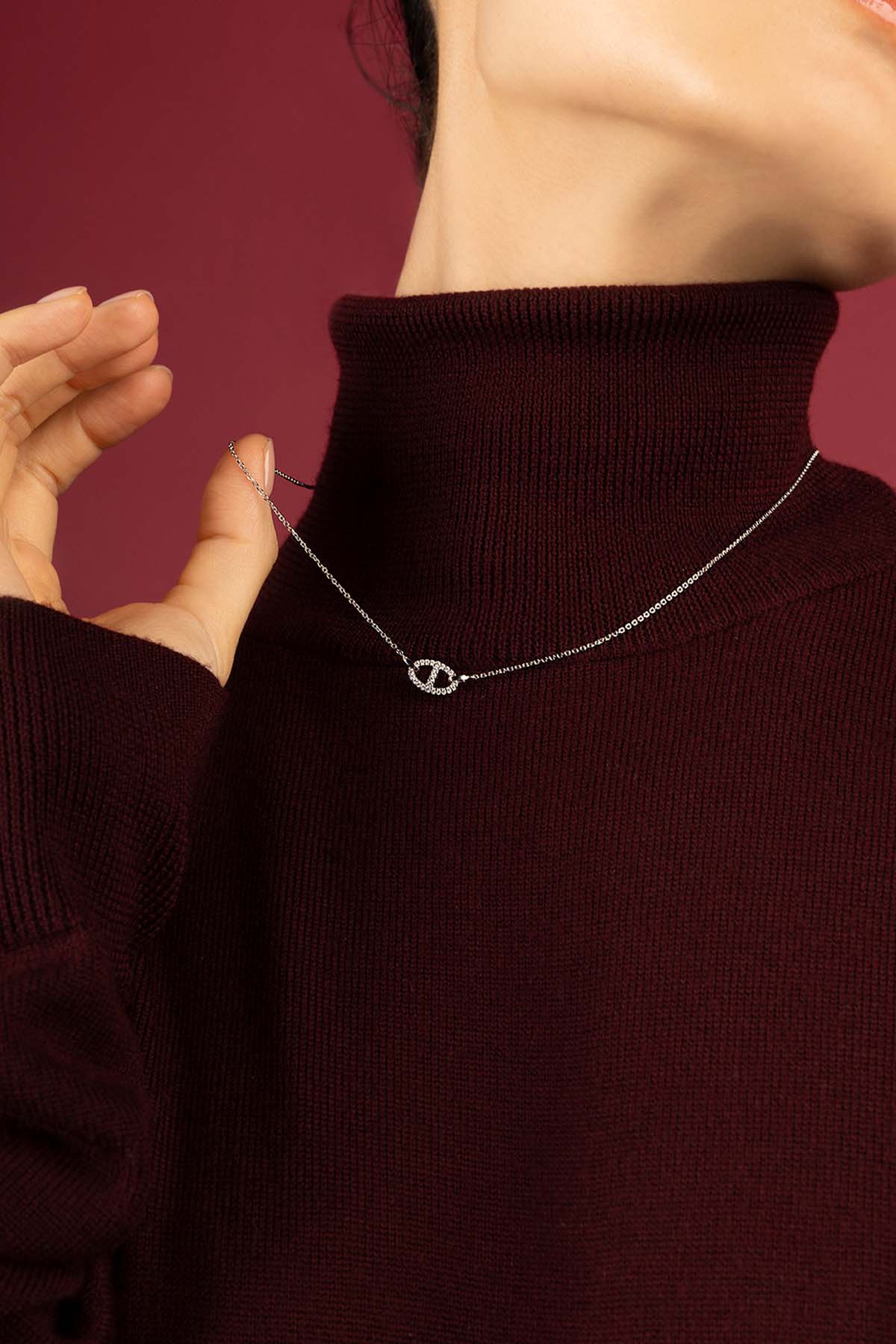 Woman wearing APM Necklace, a delicate glow against burgundy warmth.