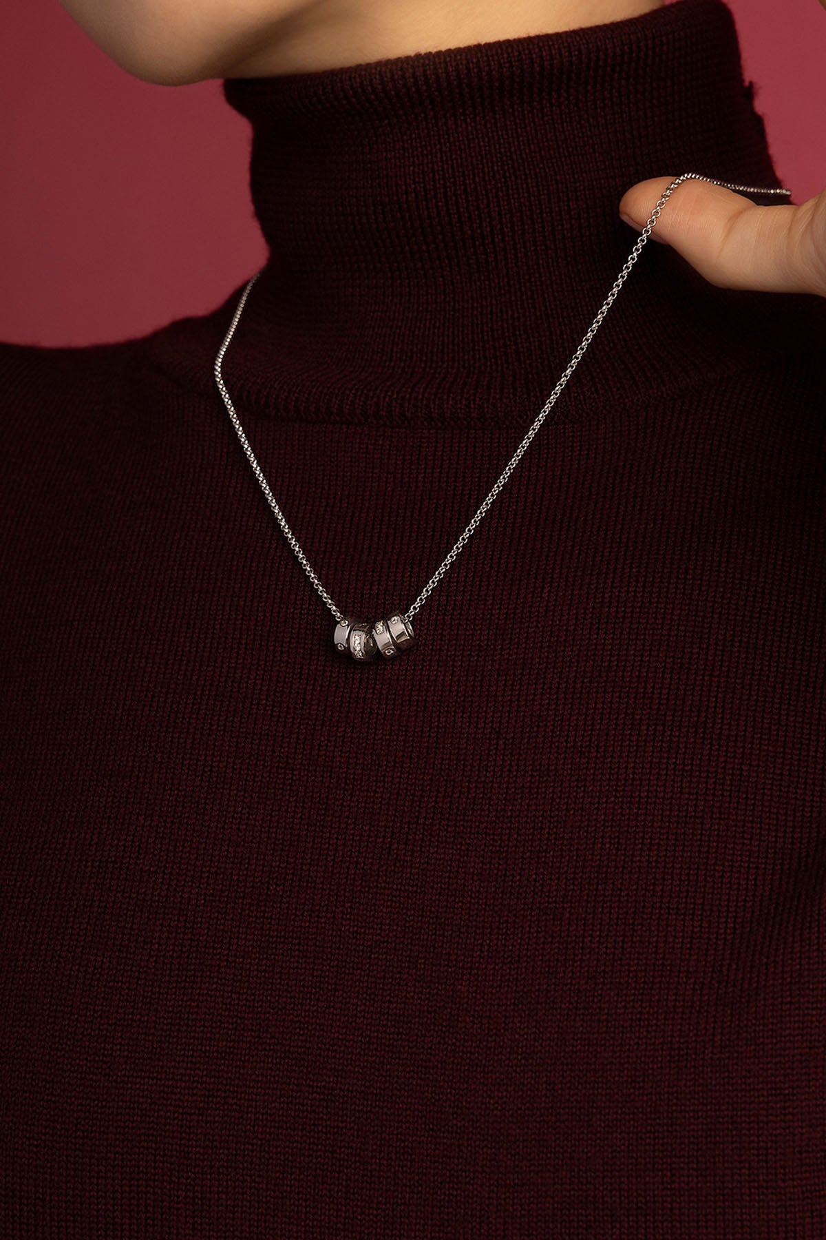 Woman wearing APM Monaco necklace, delicate charms glowing against burgundy knit.