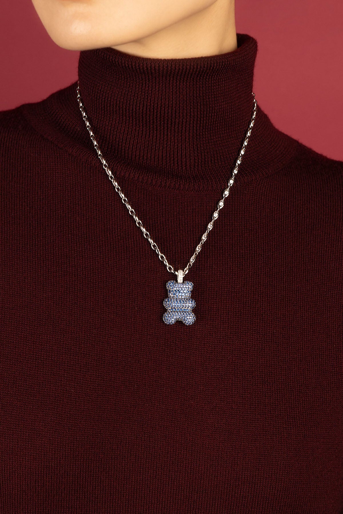Woman wearing APM Yummy Bear Necklace, a playful blue statement on cozy burgundy.