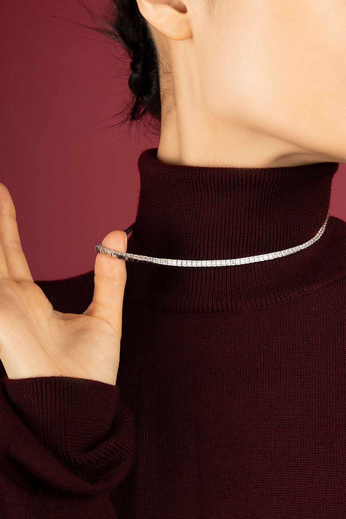 Woman wearing APM tennis necklace, a luminous line gracing burgundy knitwear with quiet elegance.