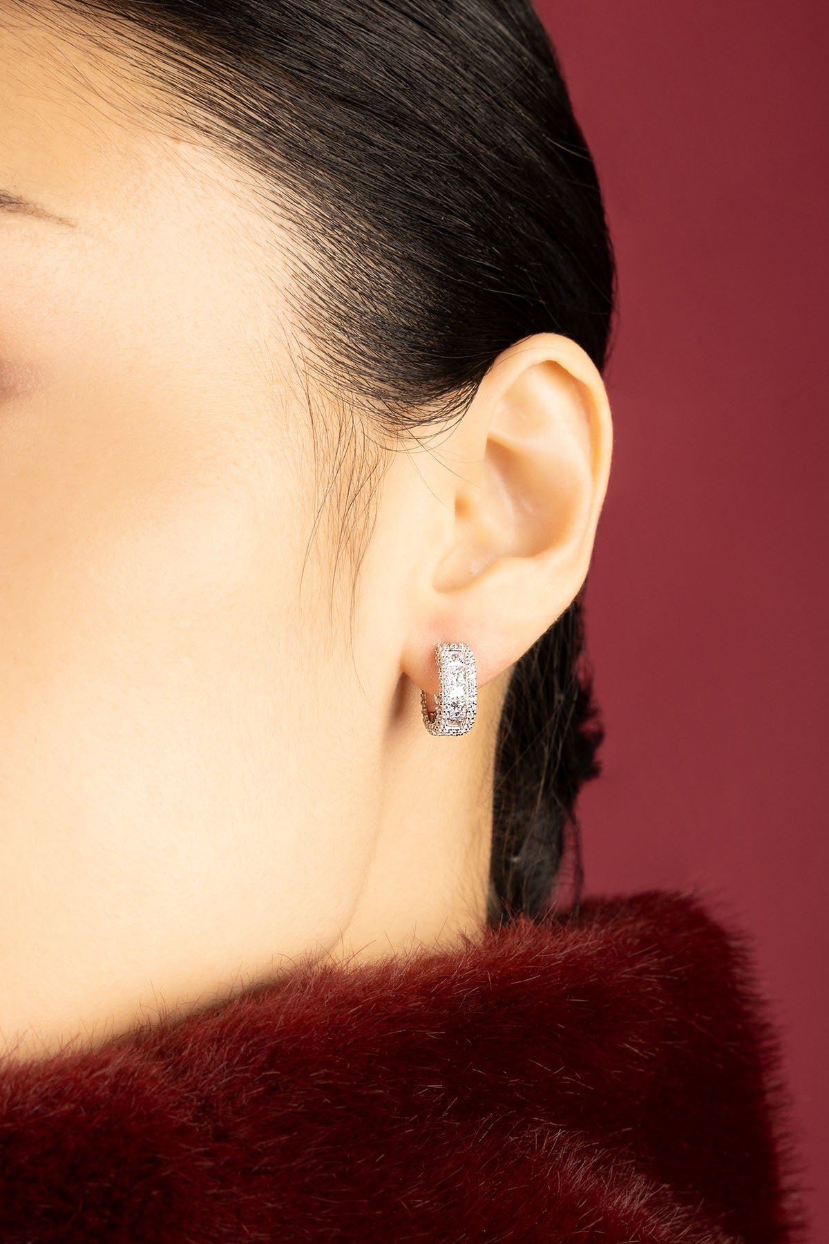 Woman wearing APM Hoop Earrings, a shimmering statement against deep crimson elegance.