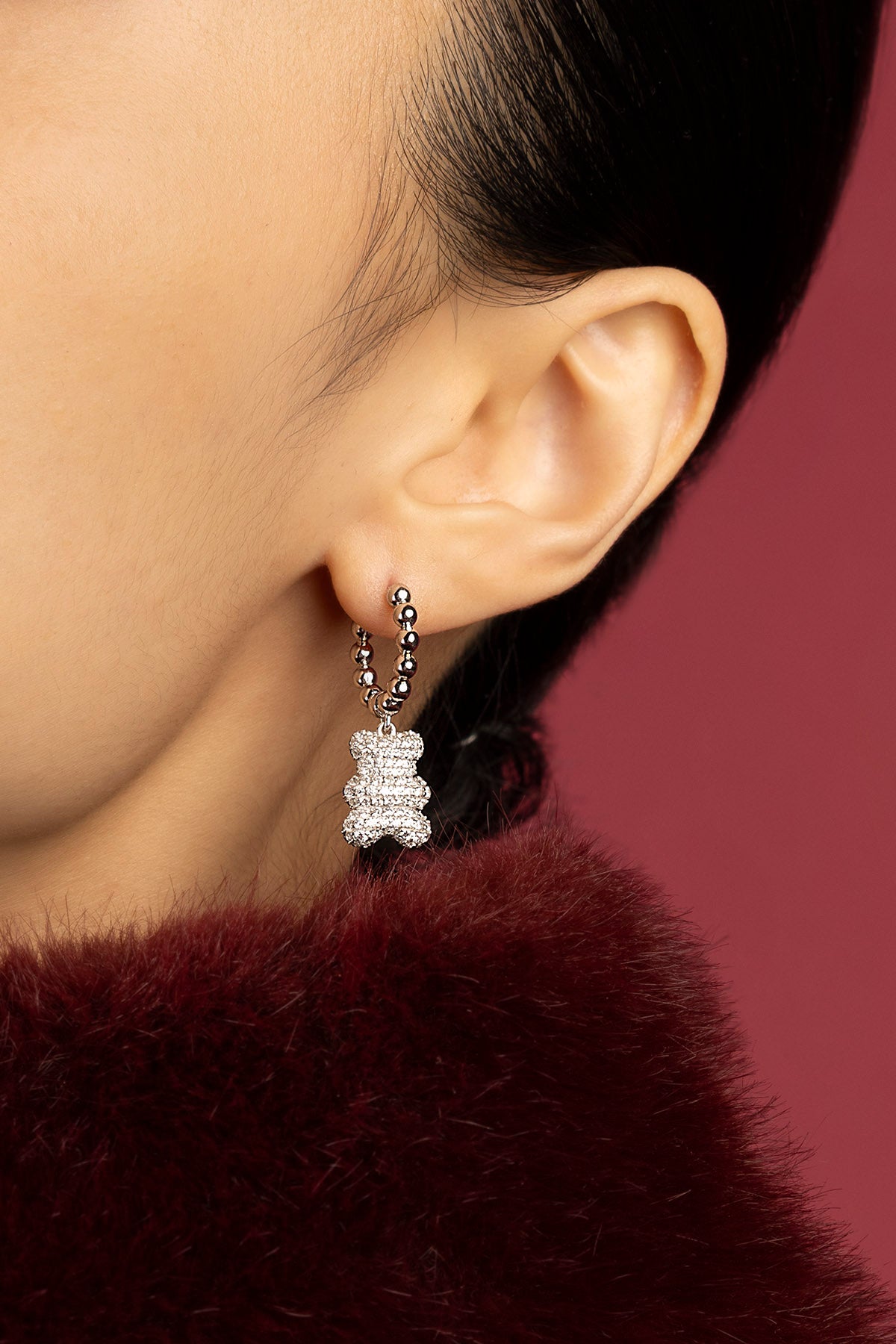 Woman wearing APM bear hoop earrings, a playful sparkle against burgundy warmth.