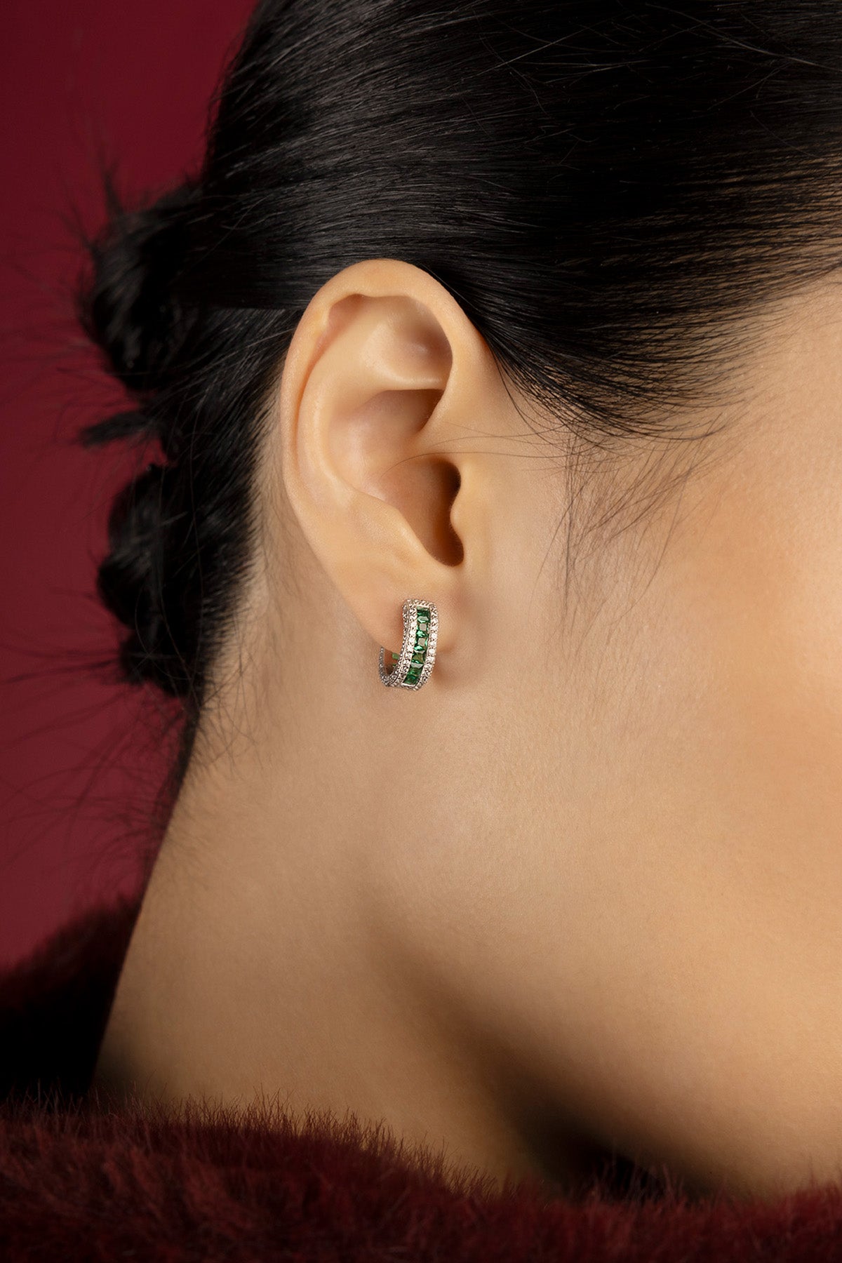 Woman wearing APM hoop earrings, a whisper of green elegance against crimson.