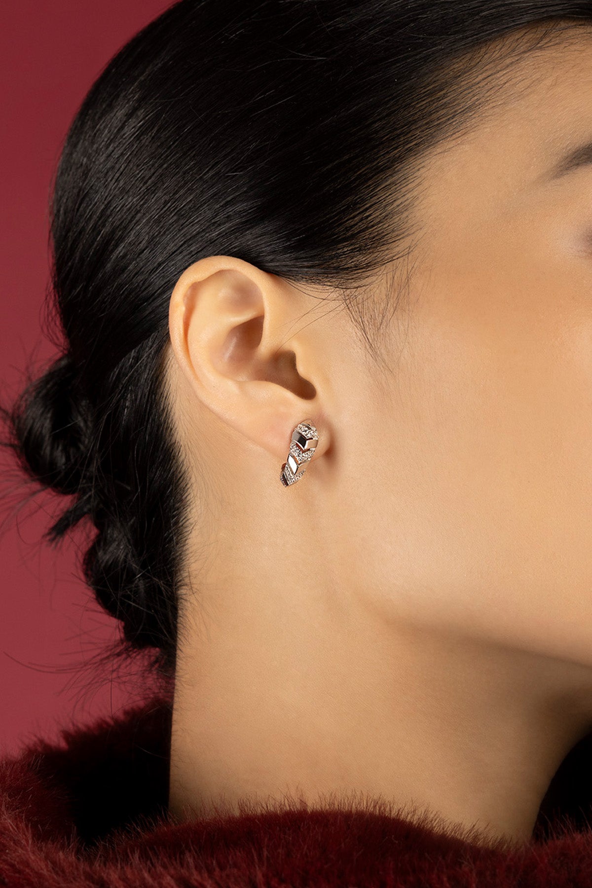 Woman wearing APM Monaco earrings, a twist of light against crimson elegance.