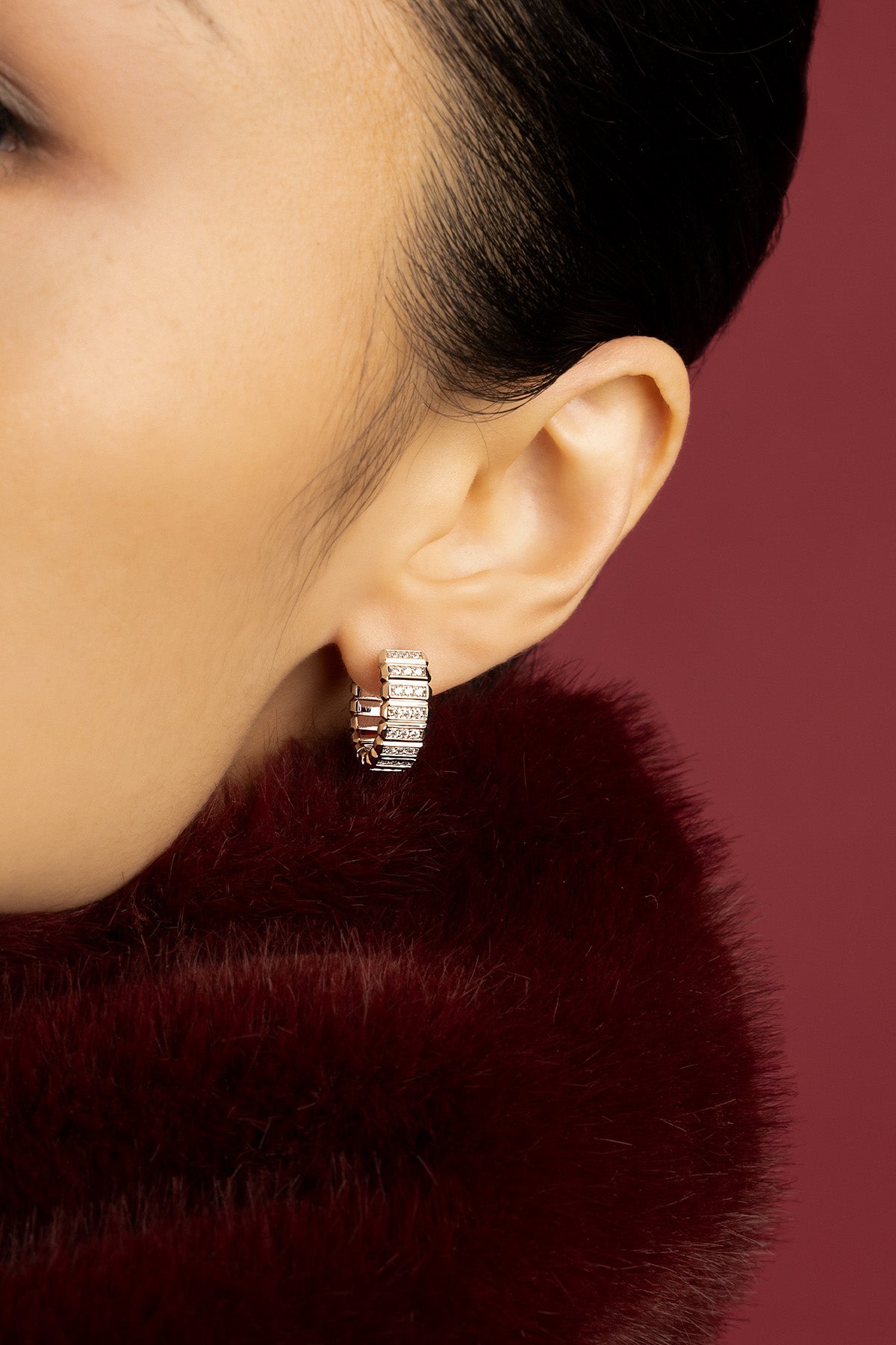 Woman wearing APM Monaco hoop earrings, a sculpted glow against burgundy softness.